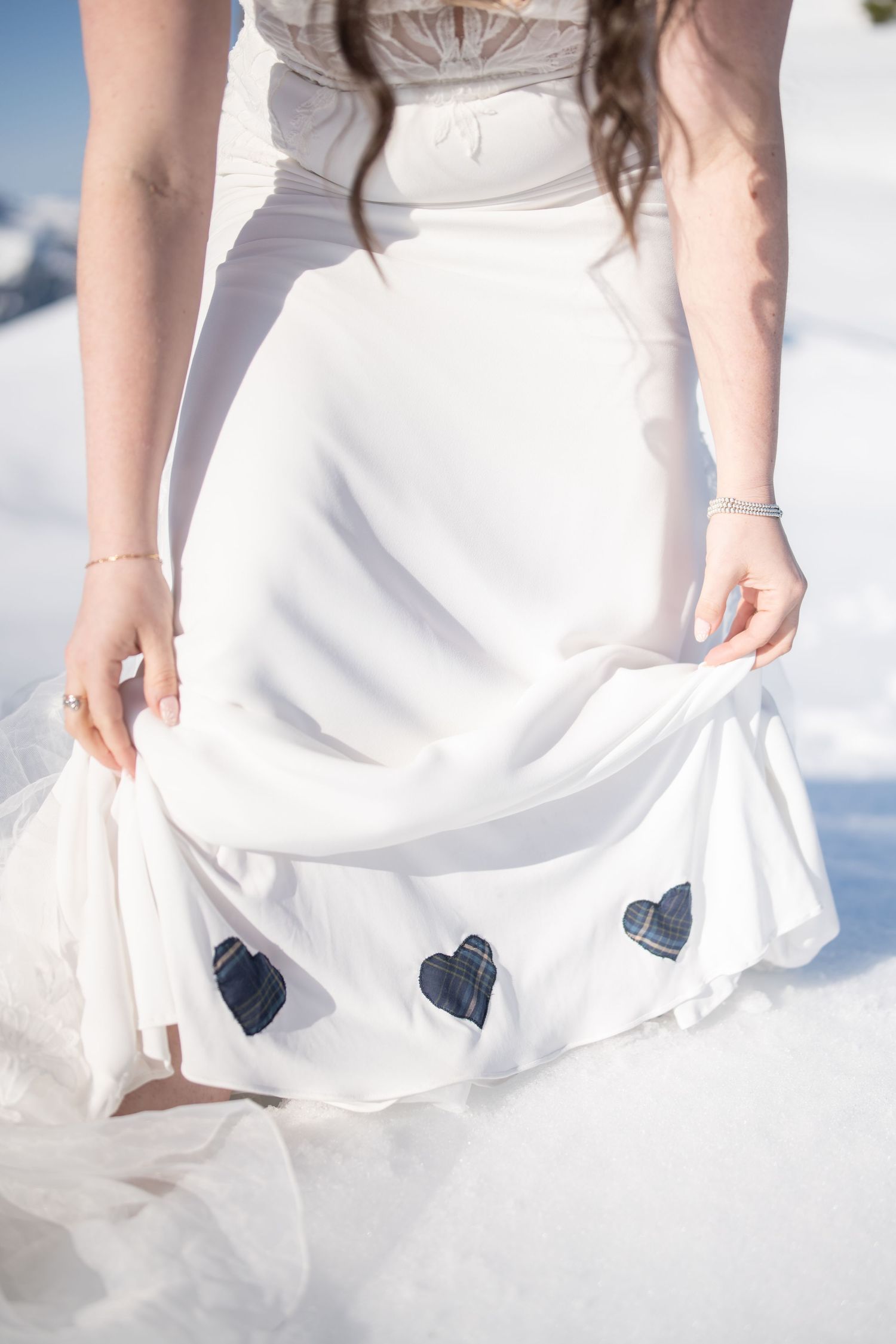 Close-up detail of a white wedding dress with small navy blue heart patches sewn on the skirt.