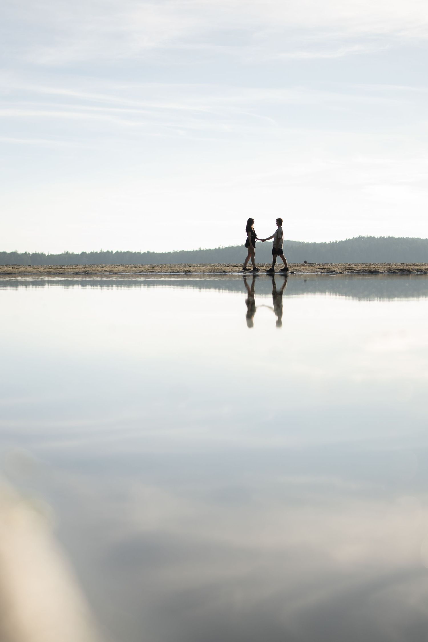 Two silhouettes reflected in still water under bright cloudy sky.