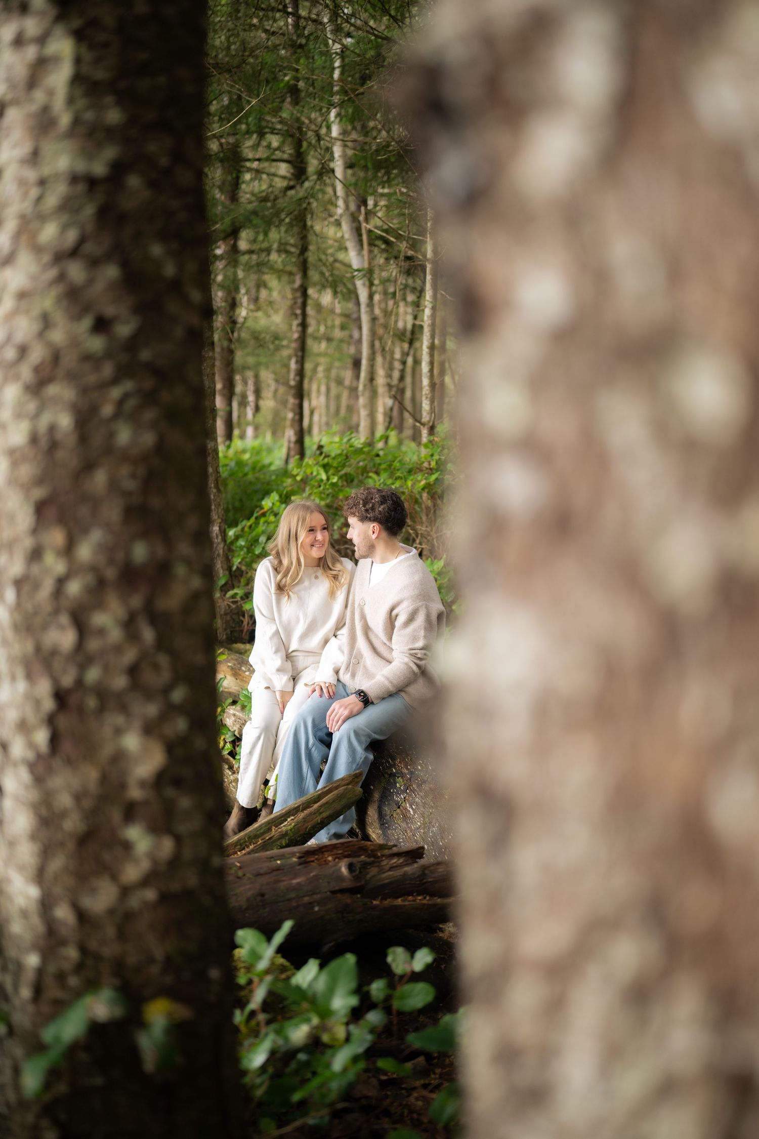 Through tree branches, a couple shares a tender moment in a forest setting.