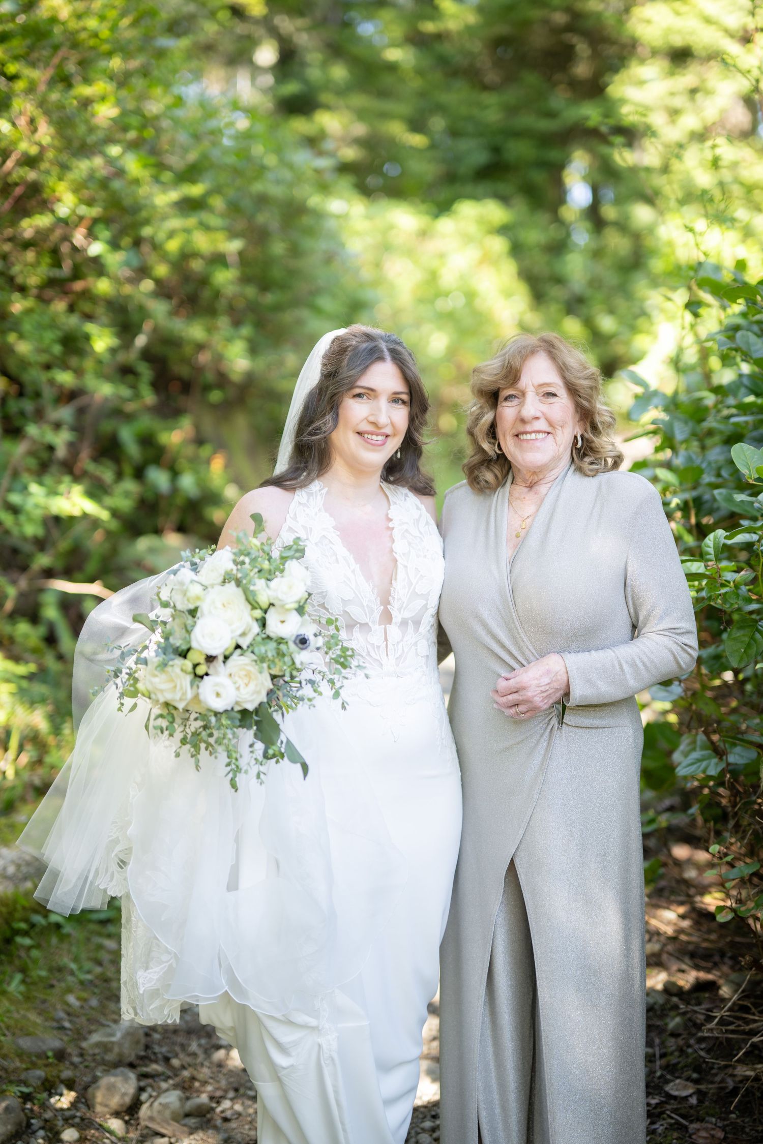 Two people in white and gray attire pose together in a lush garden setting.