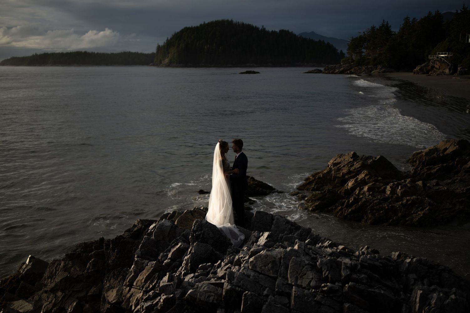Moody coastal scene with dark rocks and stormy waters at dusk.