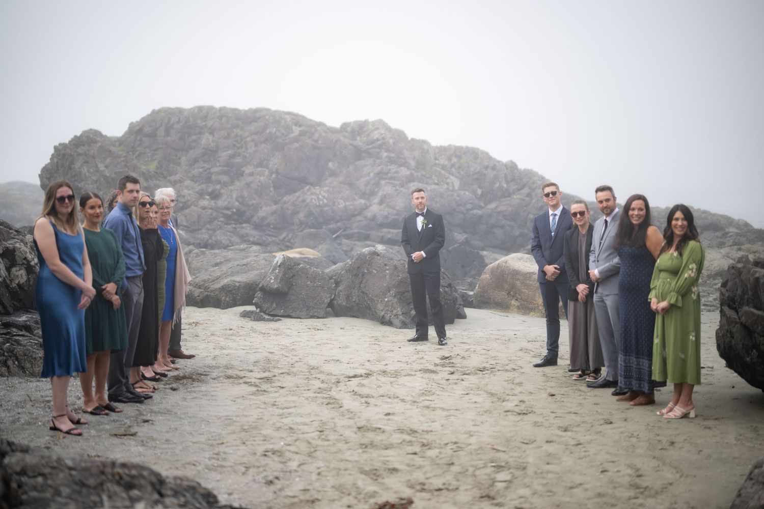 Wedding ceremony setup on a rocky beach with guests lined up on both sides.
