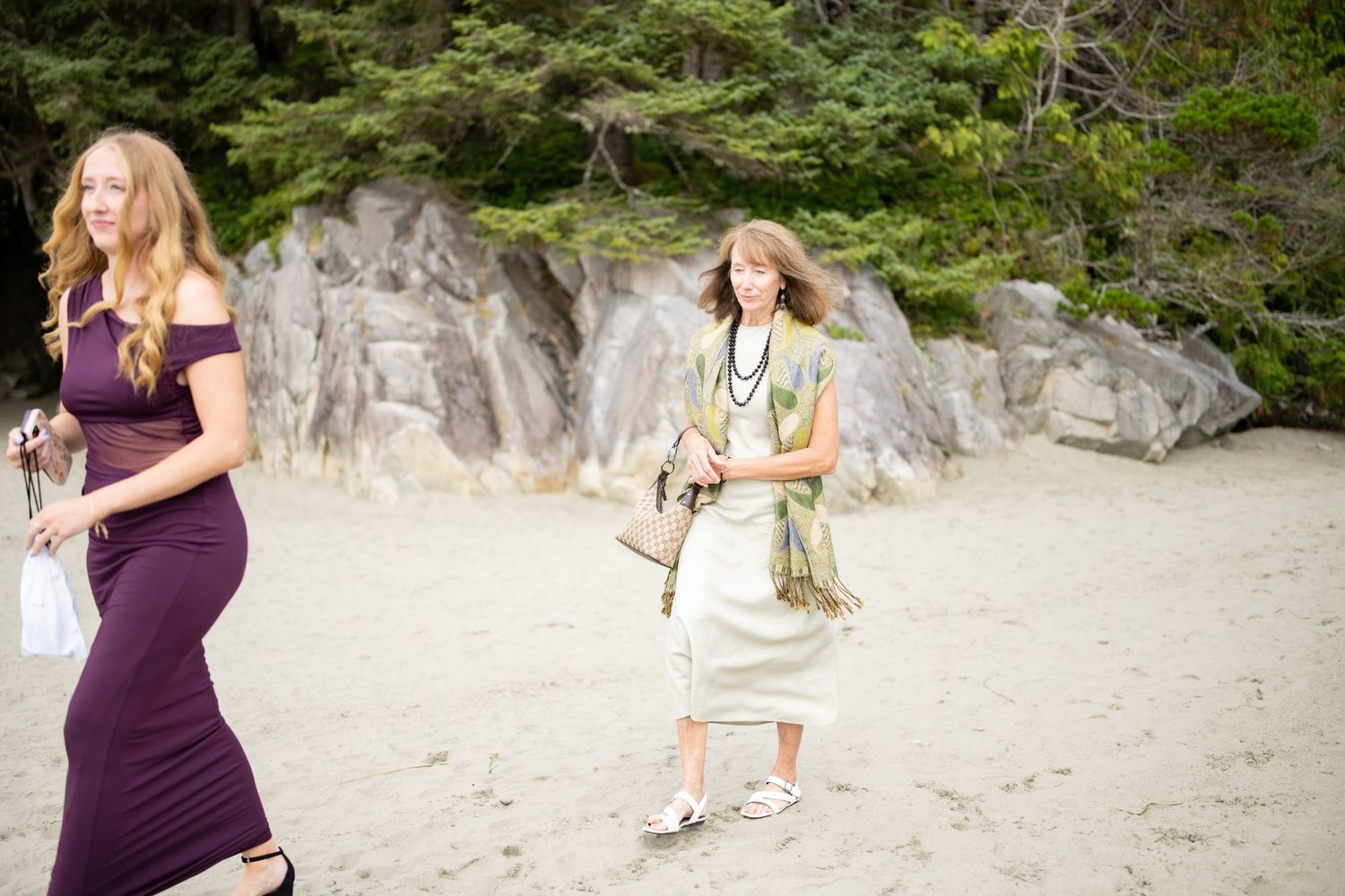 Wedding guests gather on a scenic beach with rocky cliffs in the background.
