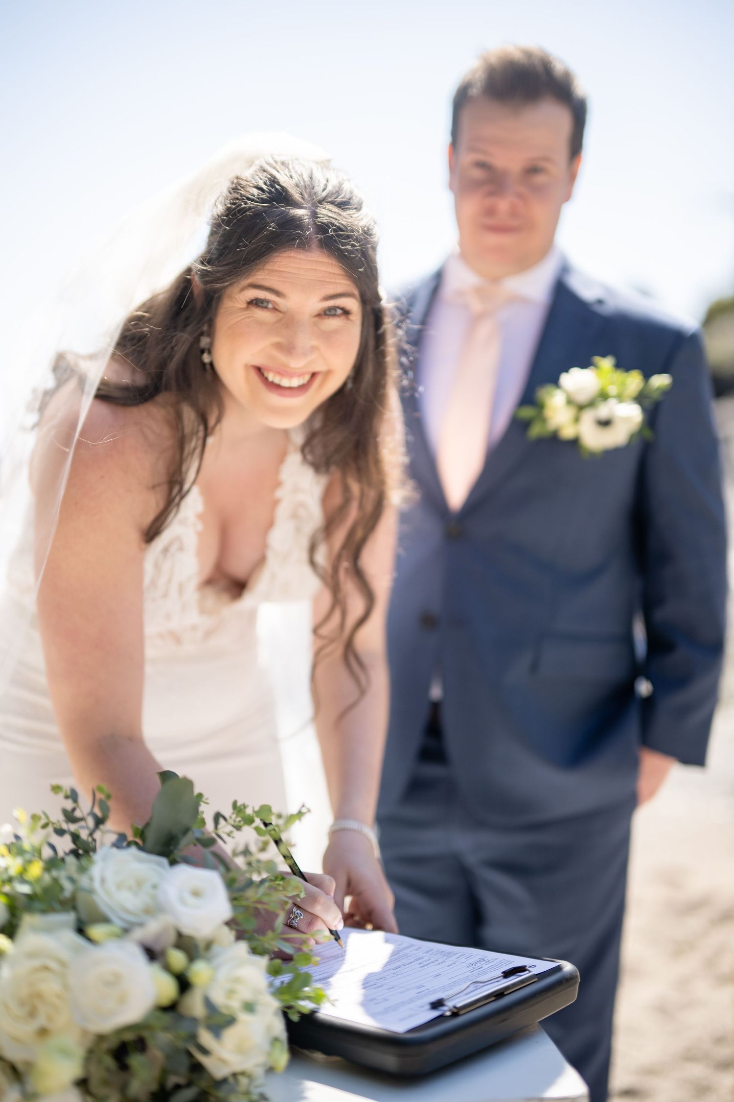 Wedding ceremony taking place outdoors with white floral bouquet and signing papers.