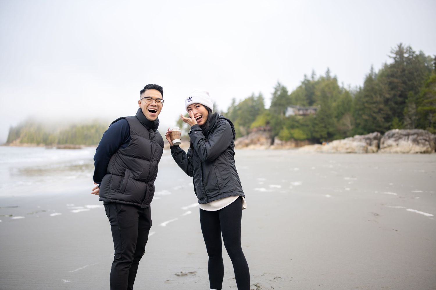 Two people sharing a playful moment on a foggy beach.