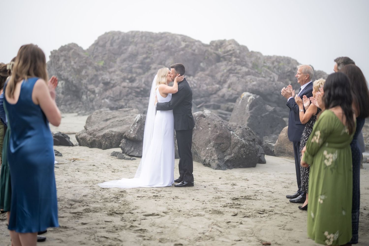 Wedding celebration unfolds on a dramatic rocky beach with attendees in formal wear.