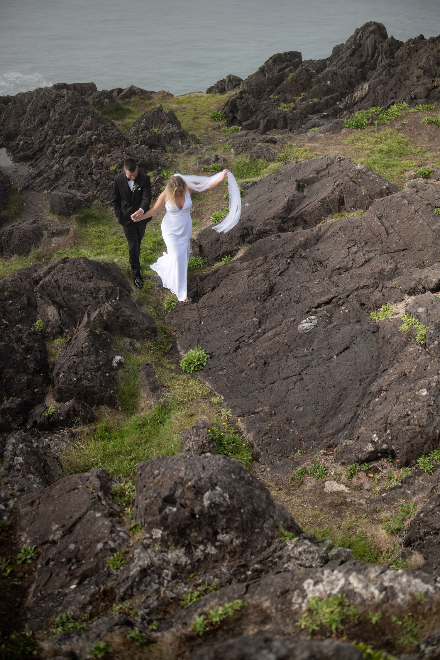 Wedding couple poses dramatically on rugged volcanic rocks by the coastline.