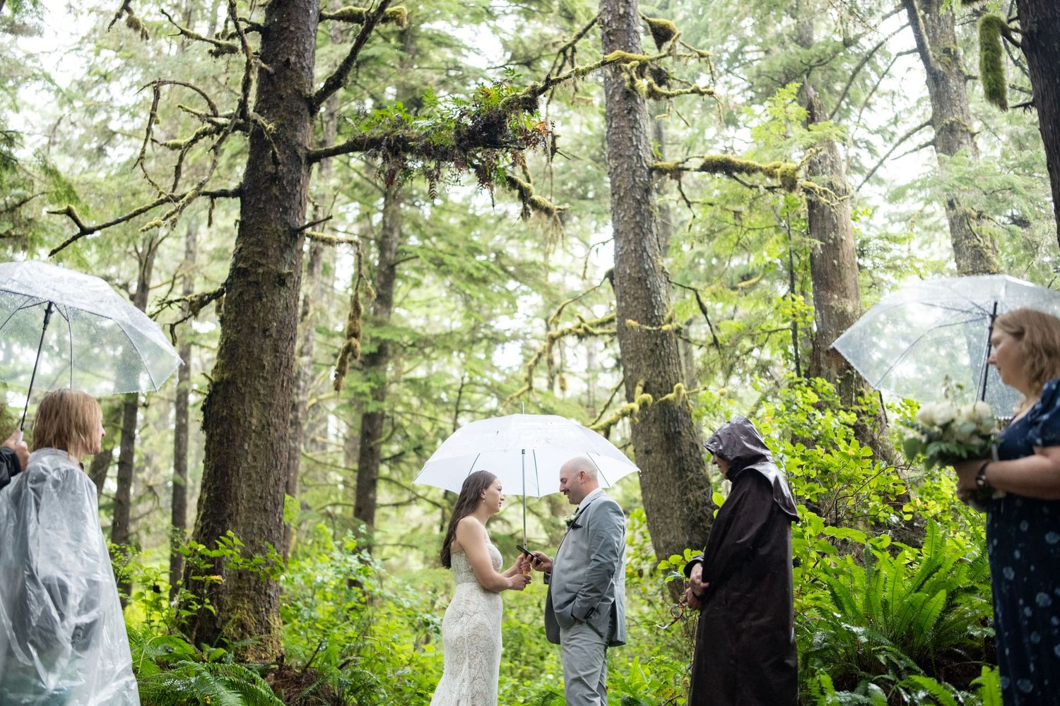 Wedding party members holding umbrellas while standing in a green forest setting.