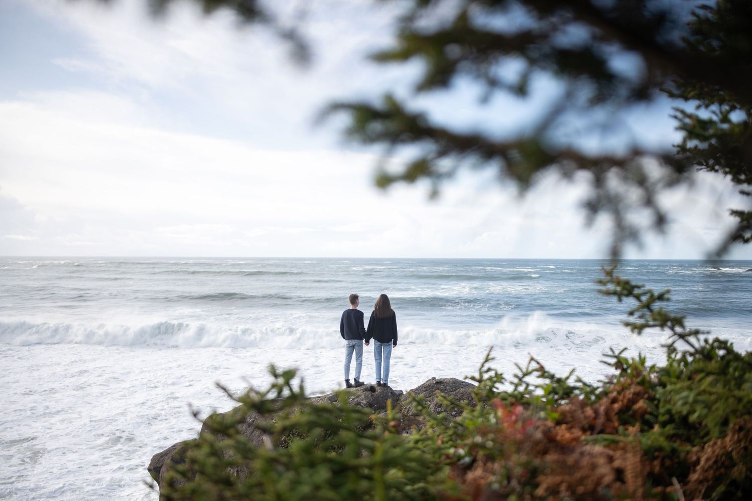 Distant view of two people standing on a coastal trail overlooking the ocean.