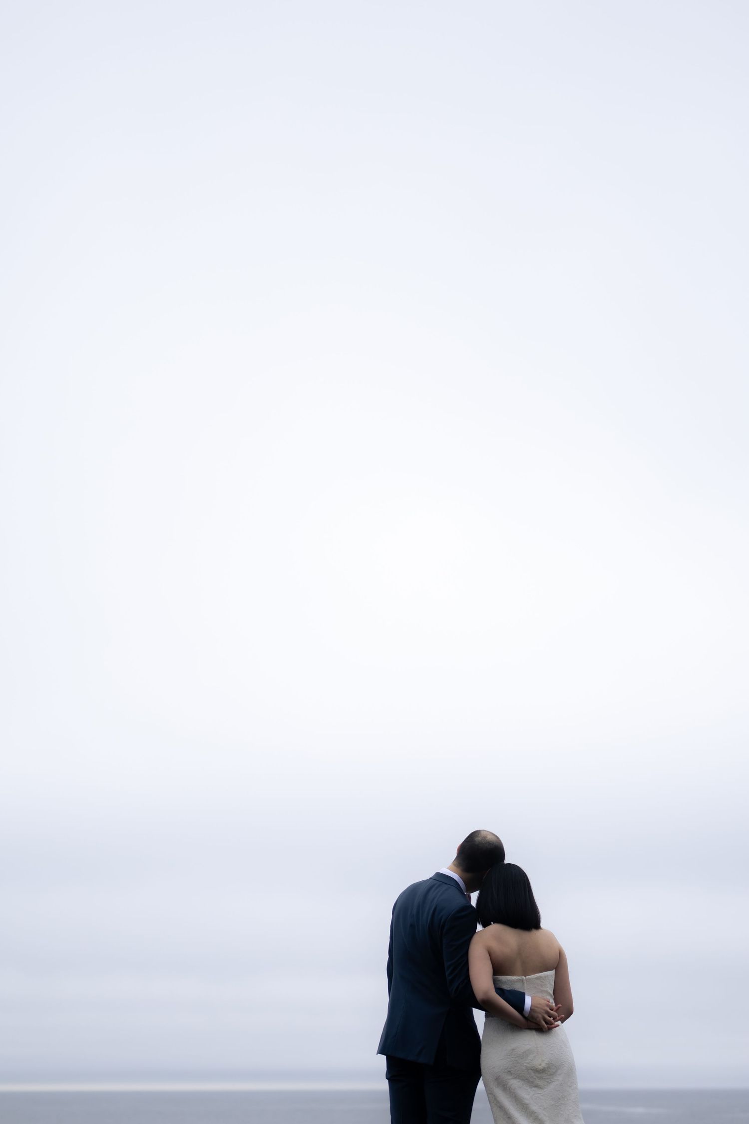 A couple stands together against a misty coastal backdrop.