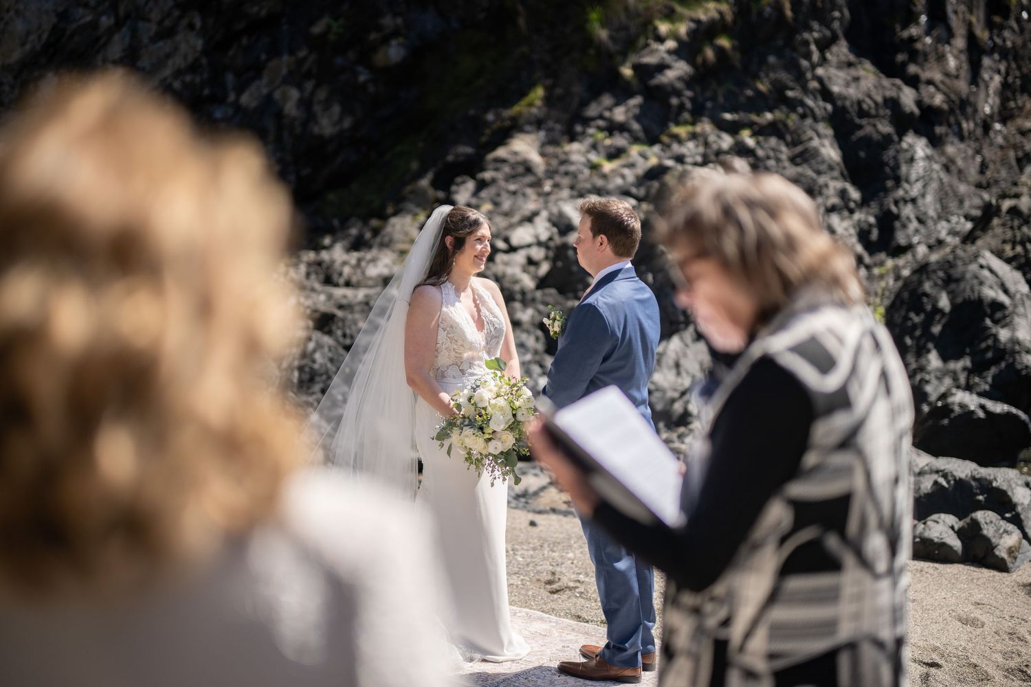 Wedding ceremony taking place on a rocky beach with ocean backdrop.