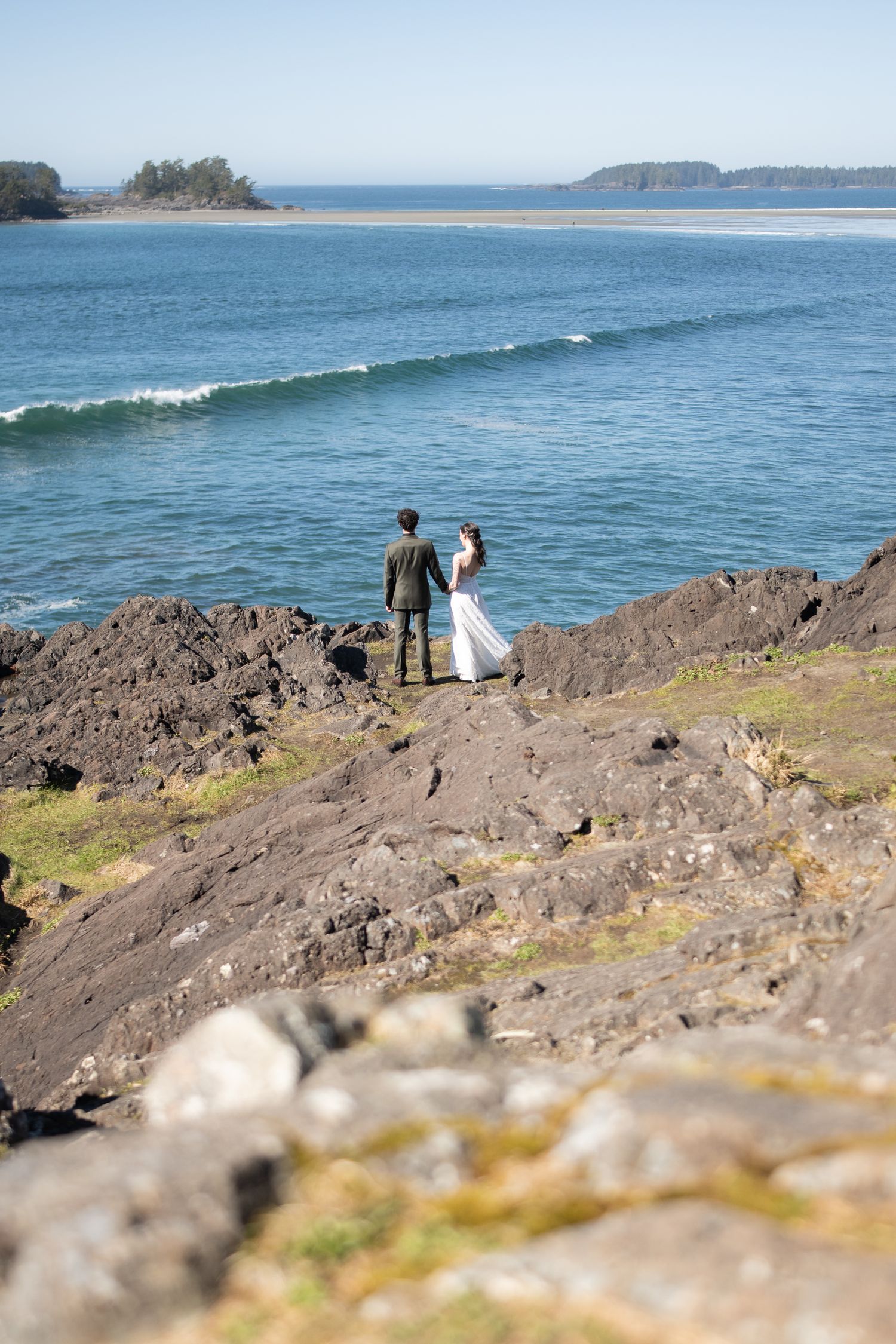 Distant view of couple sitting on rocky coastal outcrop overlooking Pacific waves.