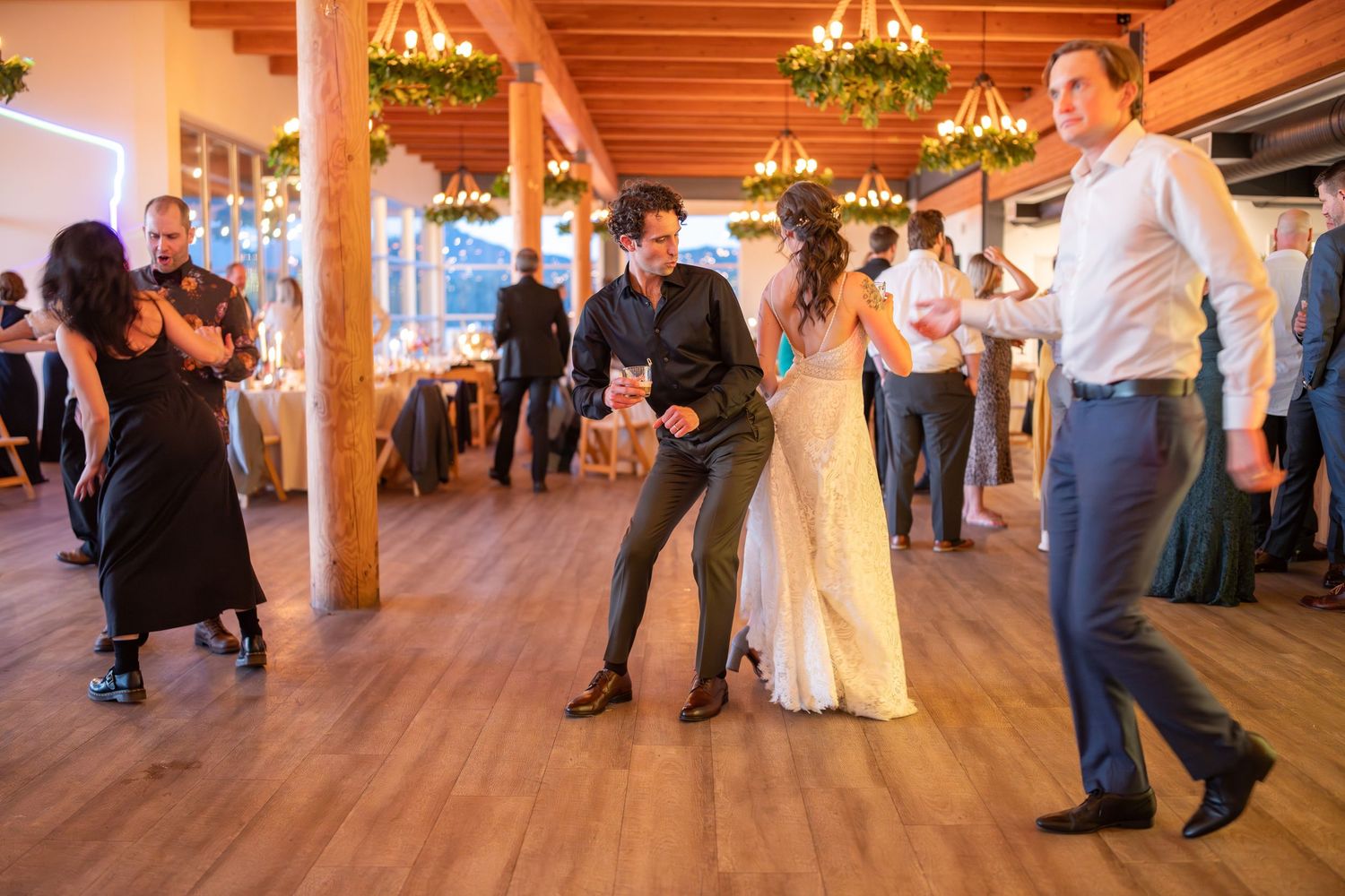 Couples dancing and celebrating in a warmly lit reception hall with wooden beams.