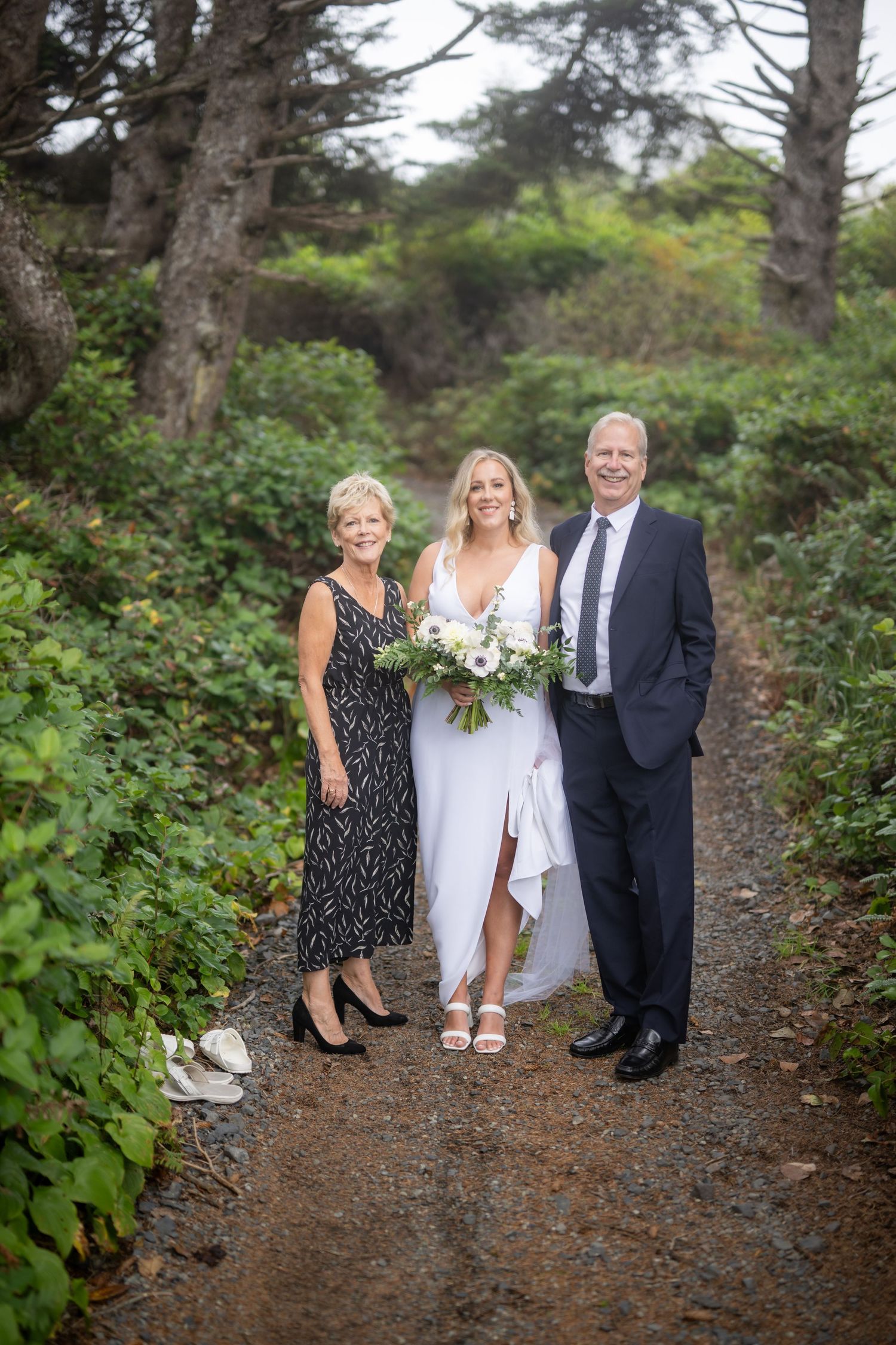 A wedding party poses on a tree-lined dirt path in formal attire.