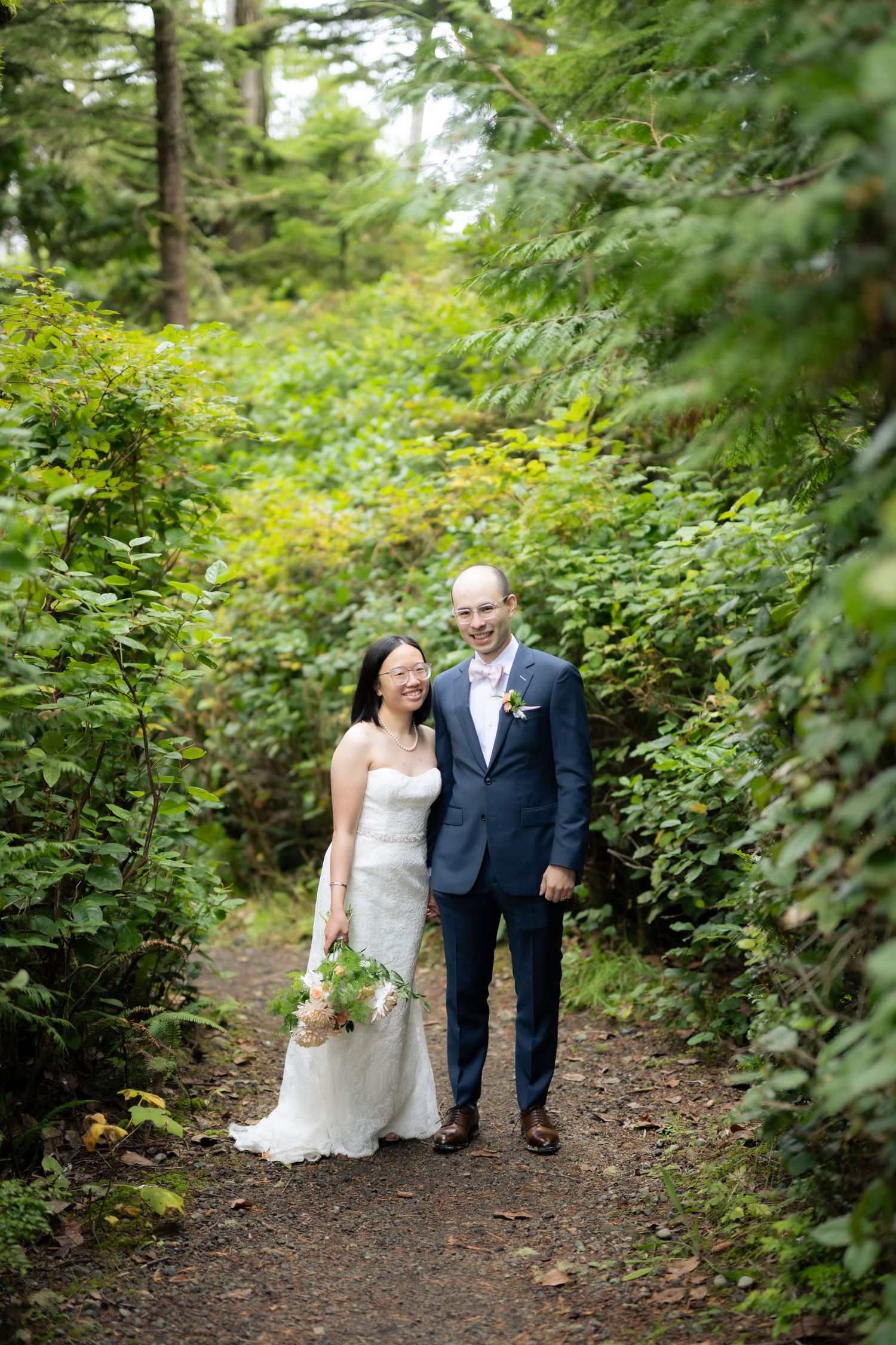 Couple walking hand in hand along a forest path surrounded by lush greenery.