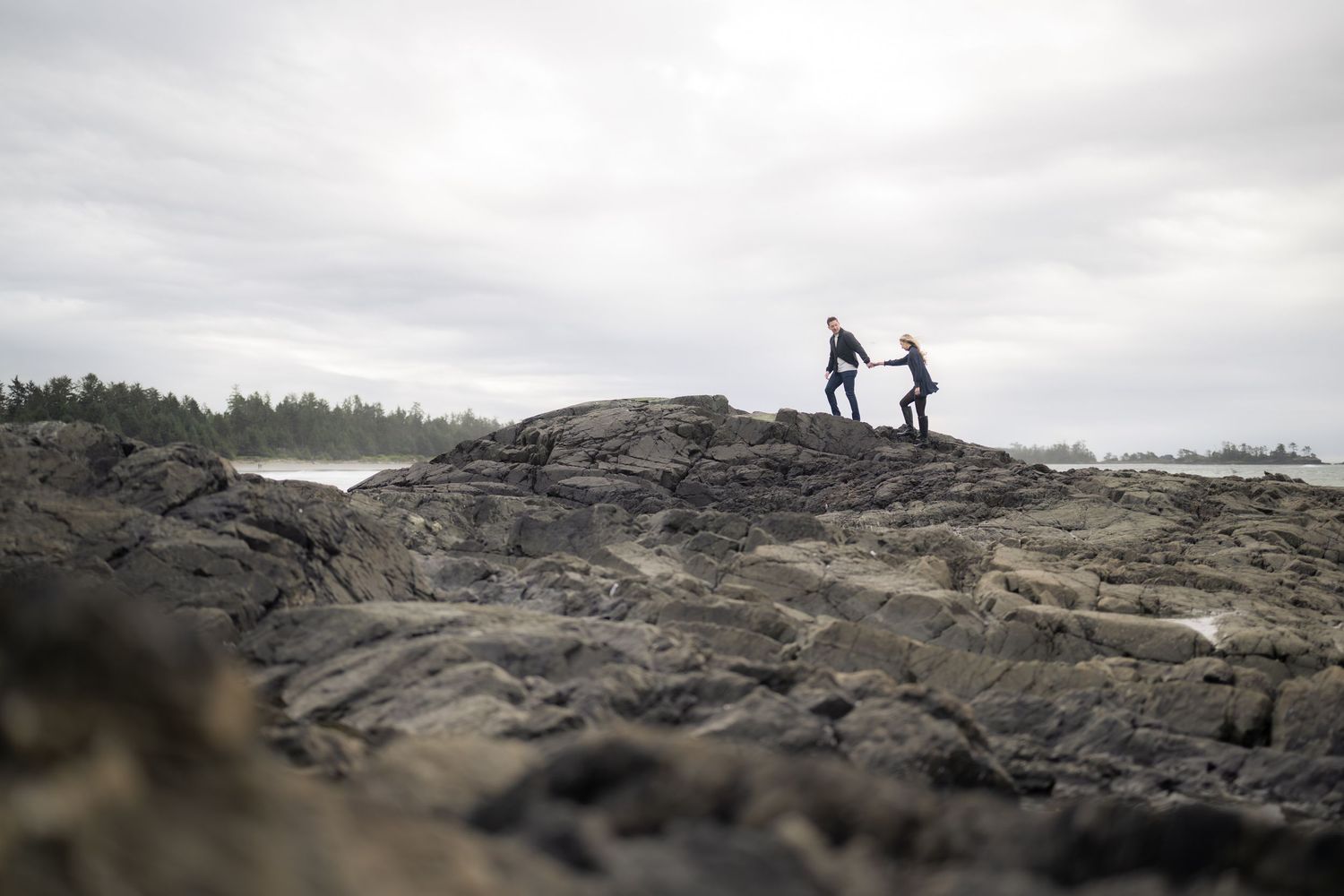 Distant figures stand on rocky coastal terrain under cloudy skies.