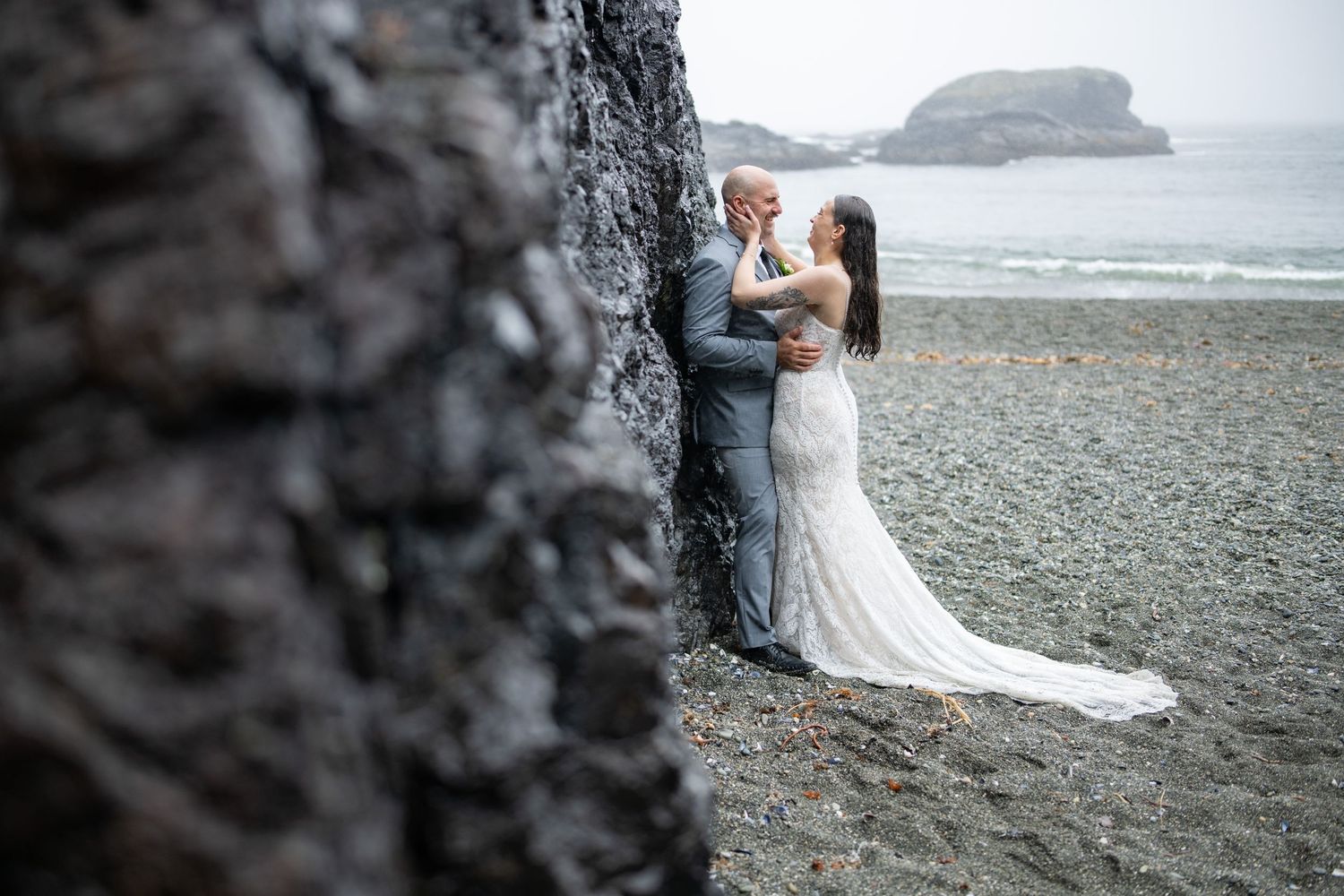 A romantic moment against a dark rocky cliff face on a moody beach landscape.