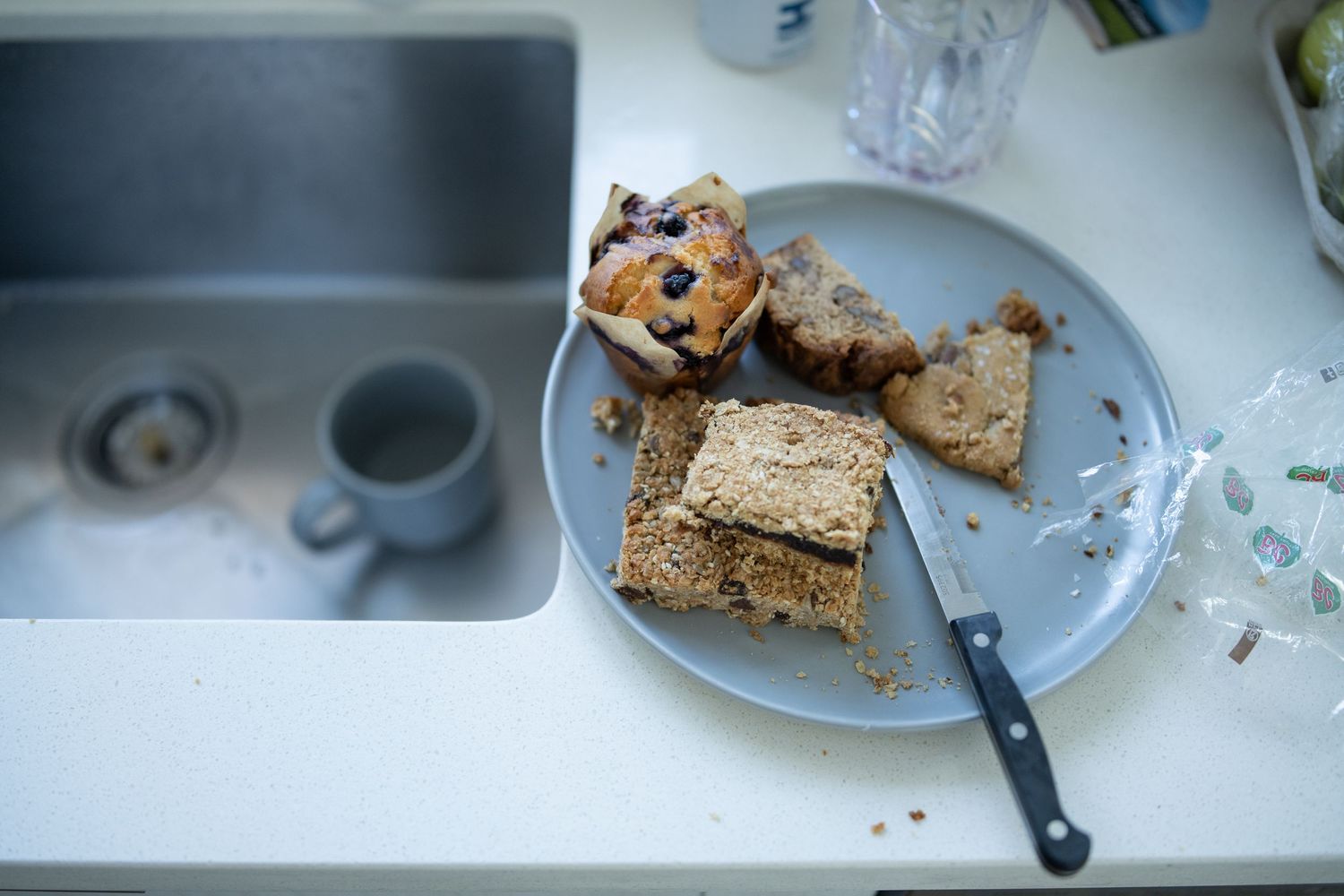 Fresh baked goods and a knife on a white plate next to a kitchen sink.