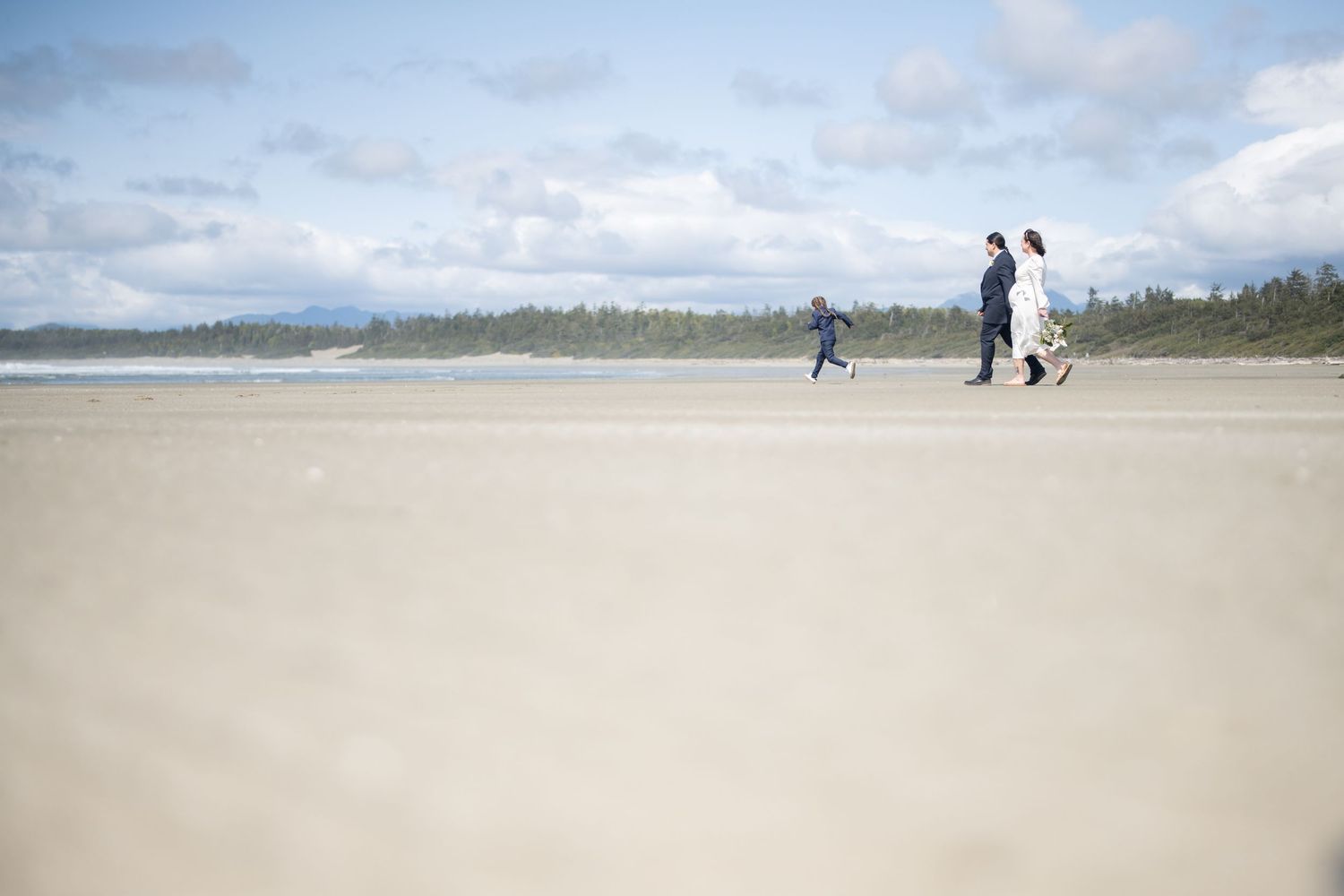 Minimalist beach scene with tiny figures walking against cloudy sky.