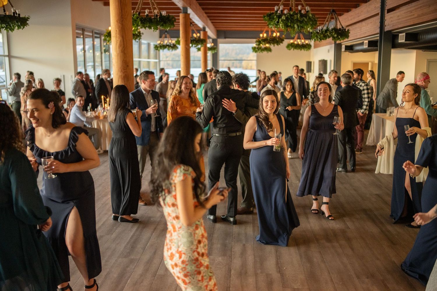 Guests enjoying a lively dance party at a wedding reception with string lights and wooden beams overhead.