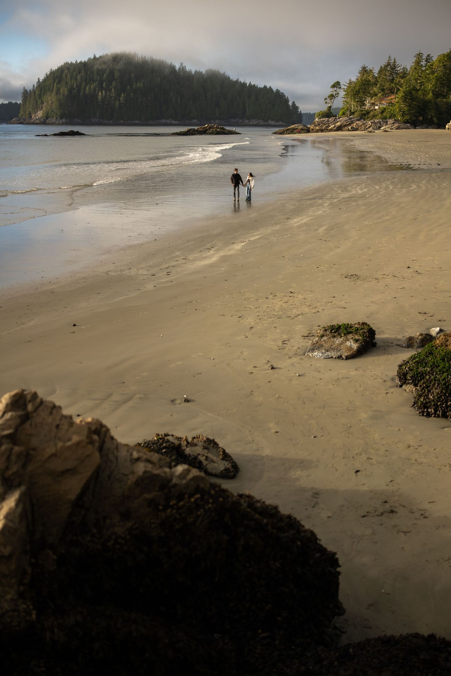 Scenic coastal beach with rocky outcrops and forested cliffs under cloudy skies.