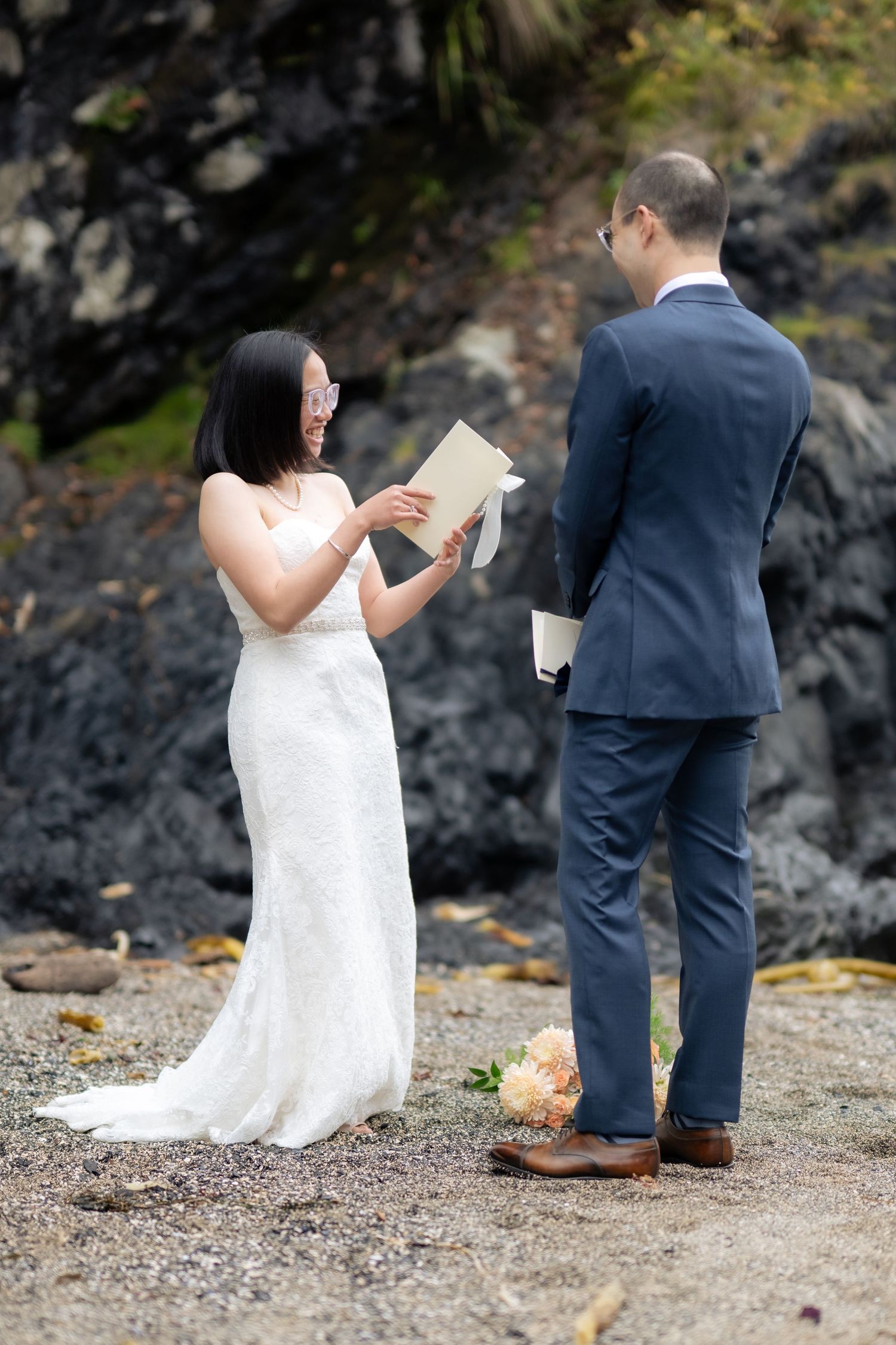 Wedding ceremony takes place on a secluded beach with dramatic coastal cliffs and evergreens.