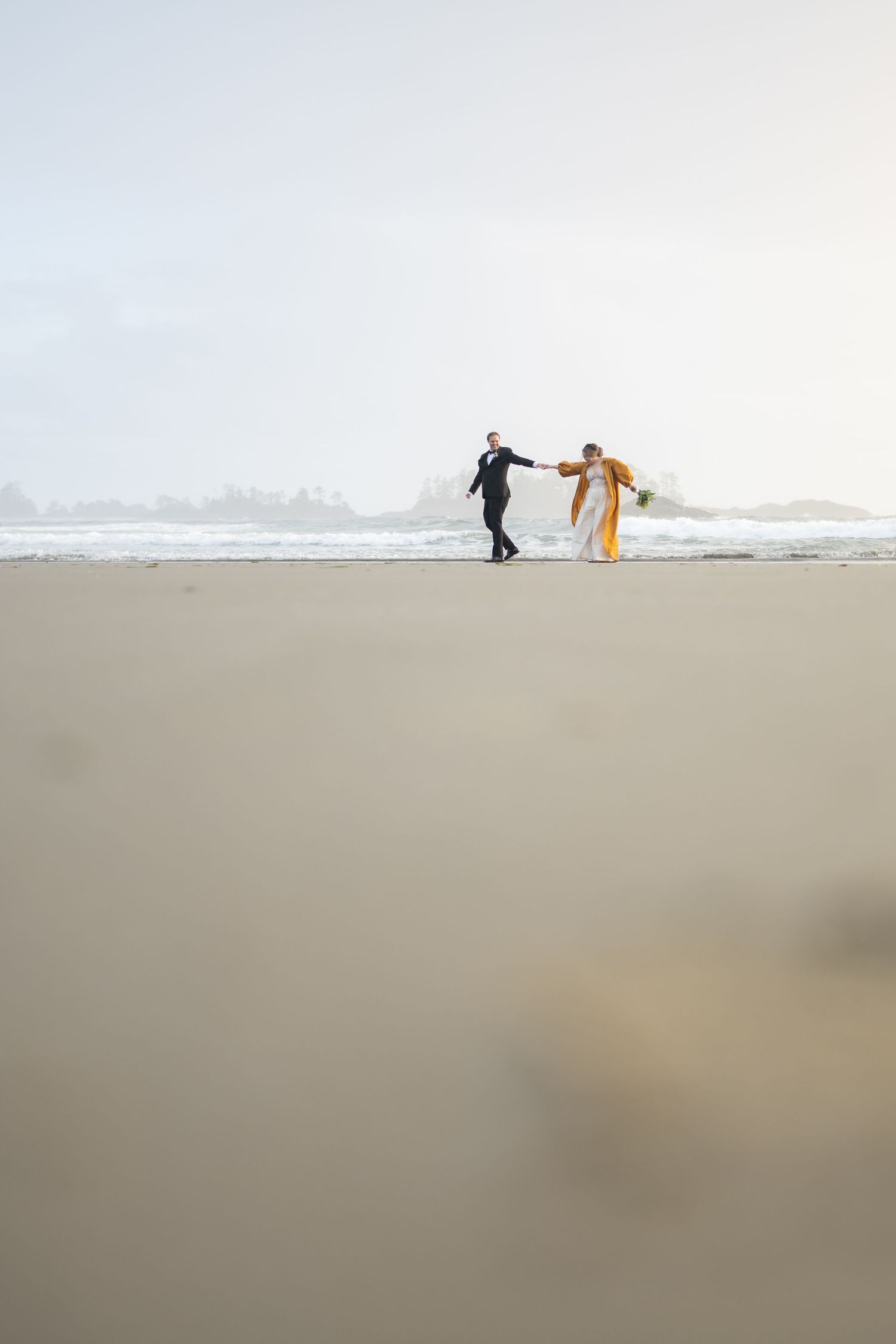 Two figures dance together on an empty beach with misty waves in the background.