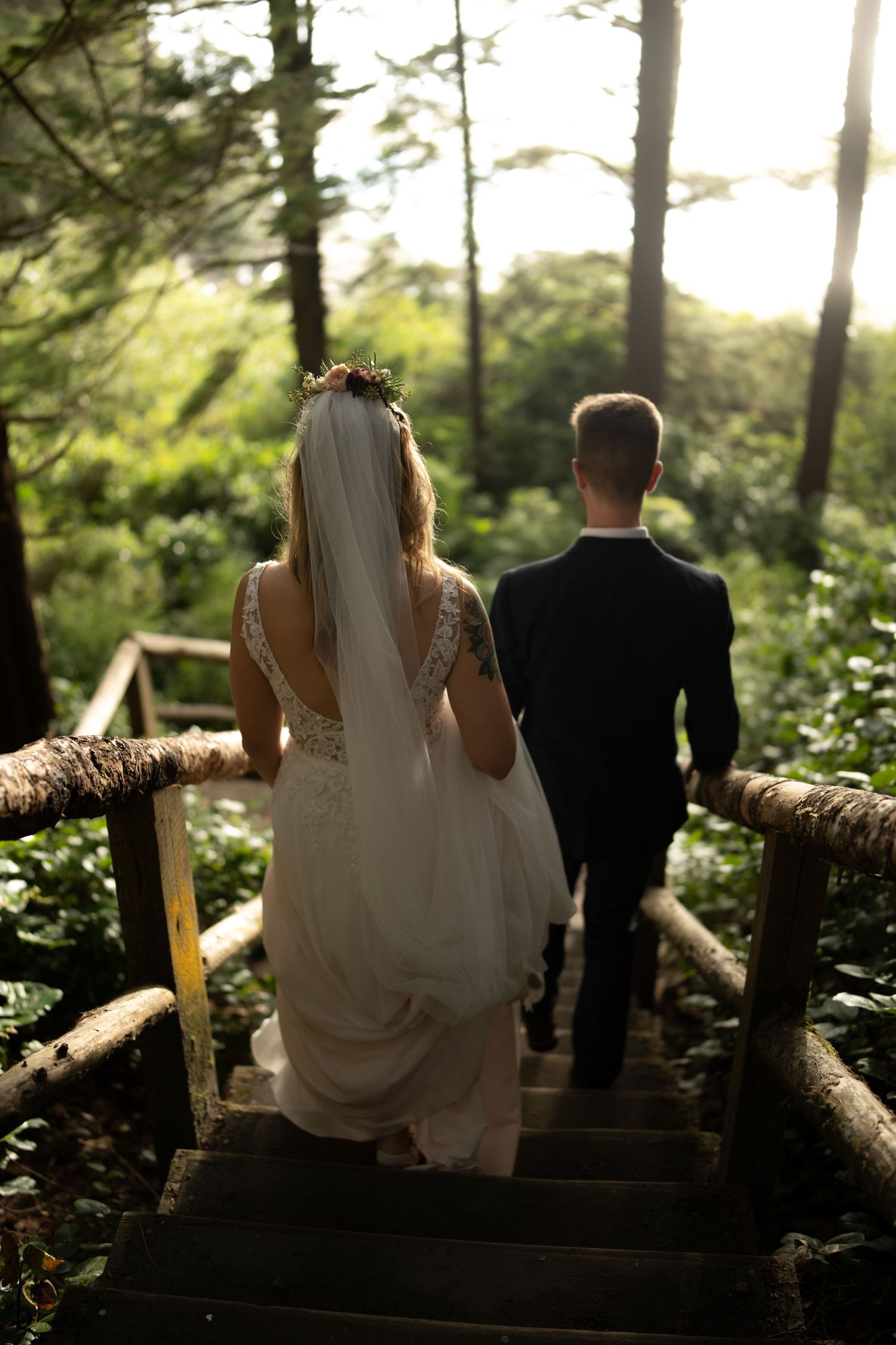 A couple sits together on a rustic log bench surrounded by lush forest greenery.