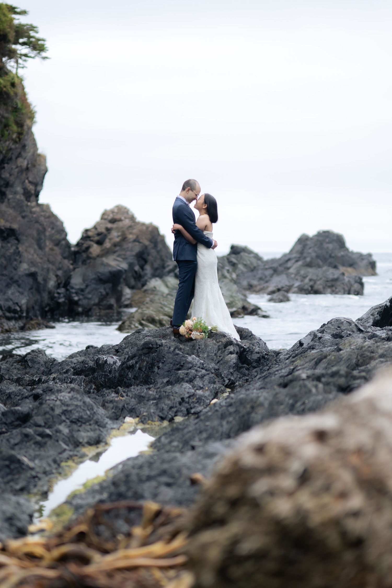 Wedding couple embracing on dramatic black volcanic rocks overlooking the ocean.
