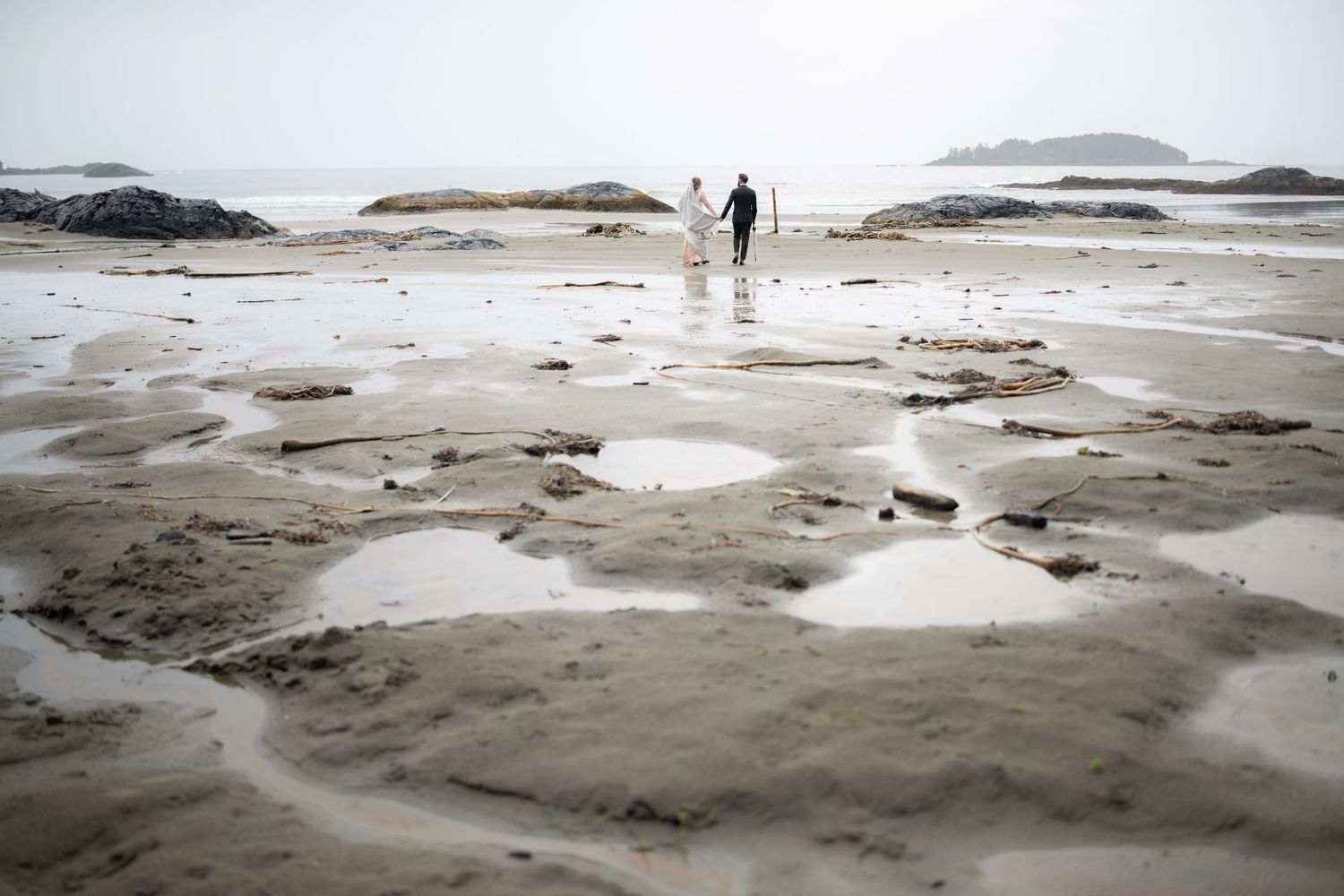 Misty coastal beach landscape with tidal pools and distant islands.