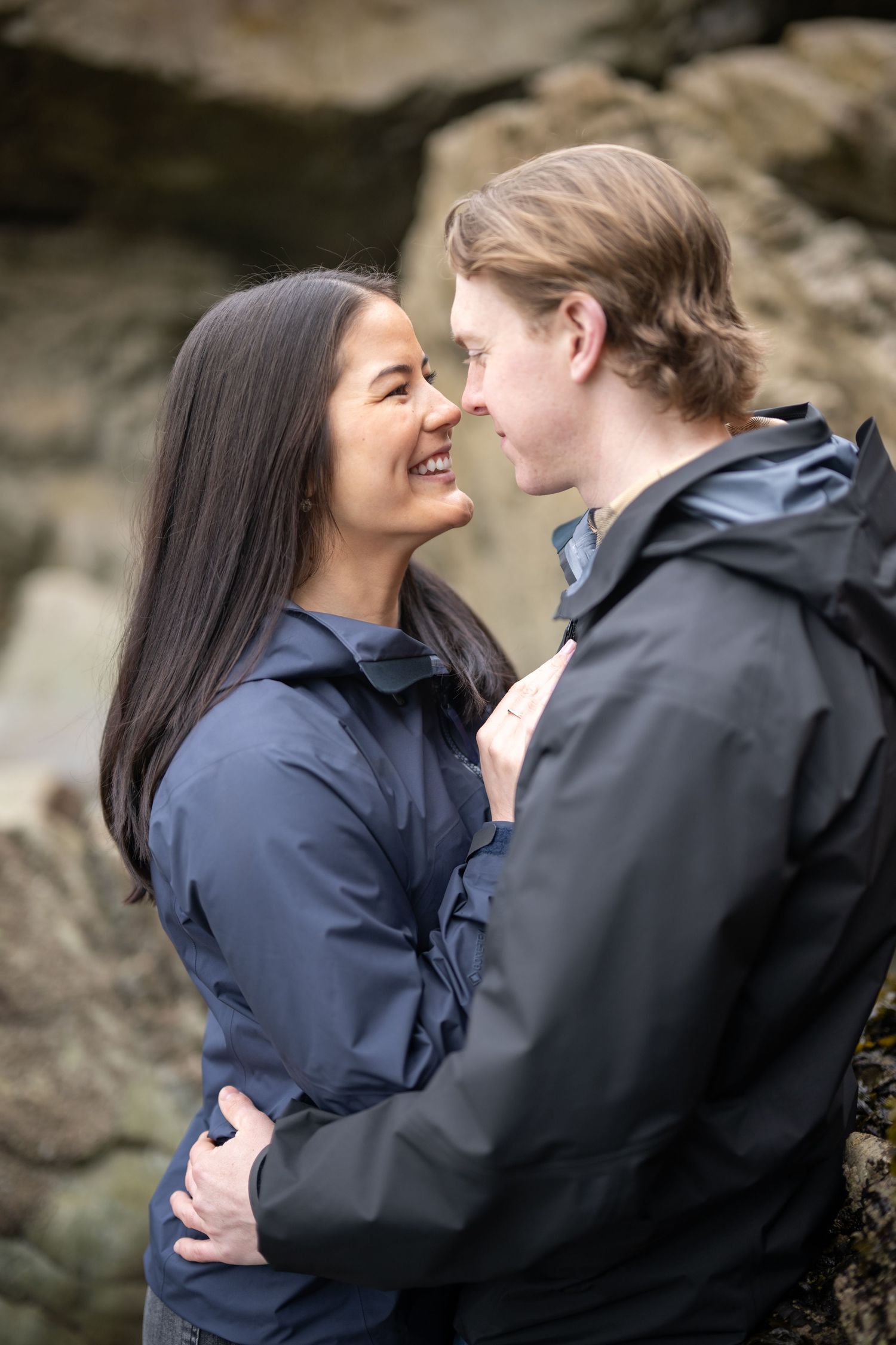 A joyful intimate moment shared between two people in navy jackets against rocky cliffs.