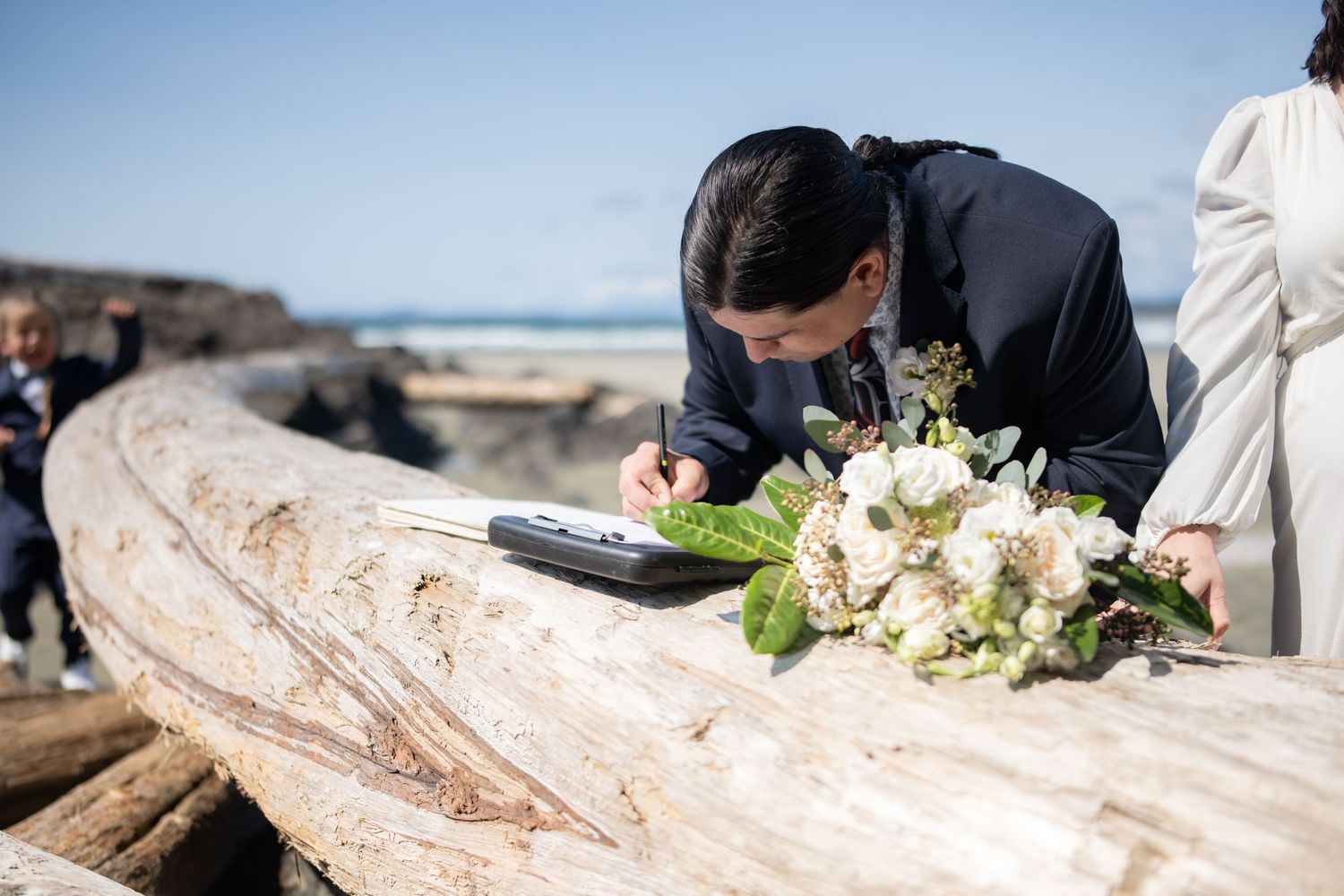 Wedding decorations and floral arrangements placed on natural driftwood at a beach ceremony.