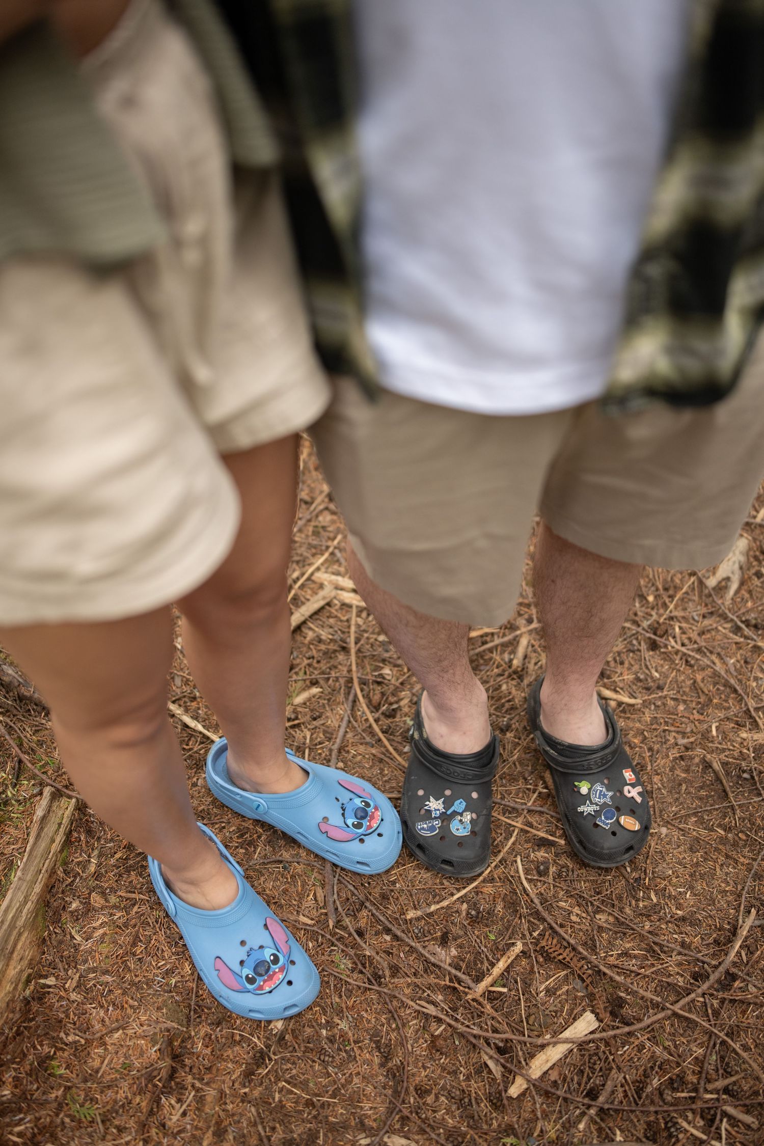 Two pairs of feet wearing matching floral slippers on a forest floor.