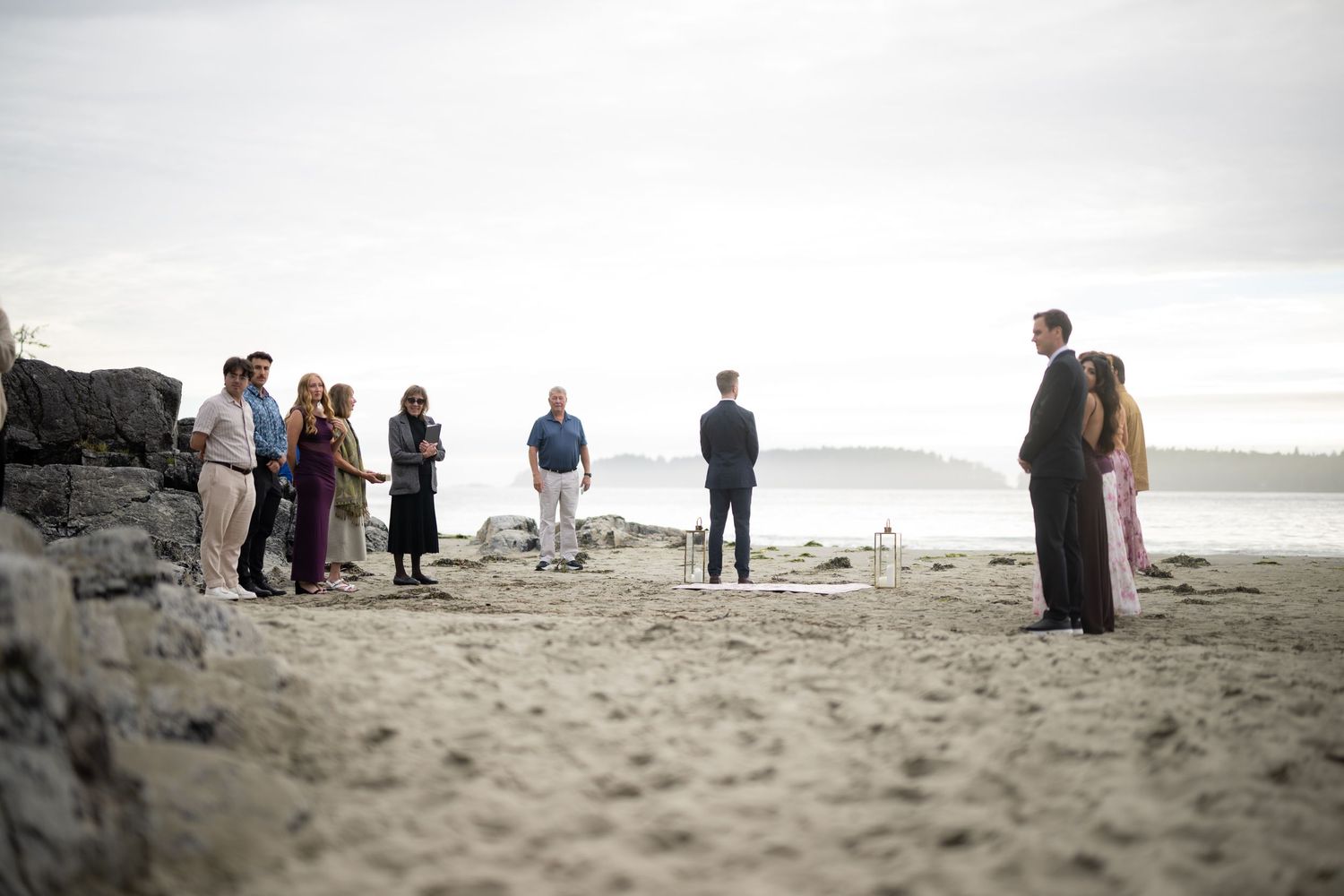 Small groups of people stand scattered along a misty beach shoreline.