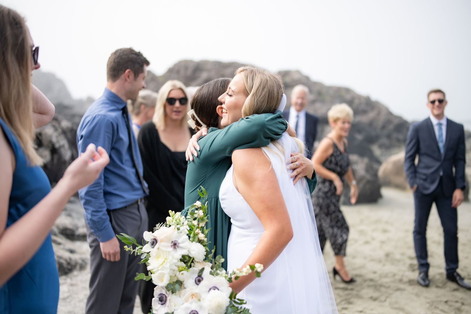 Elegant beach wedding ceremony with white floral bouquets against misty coastal backdrop.