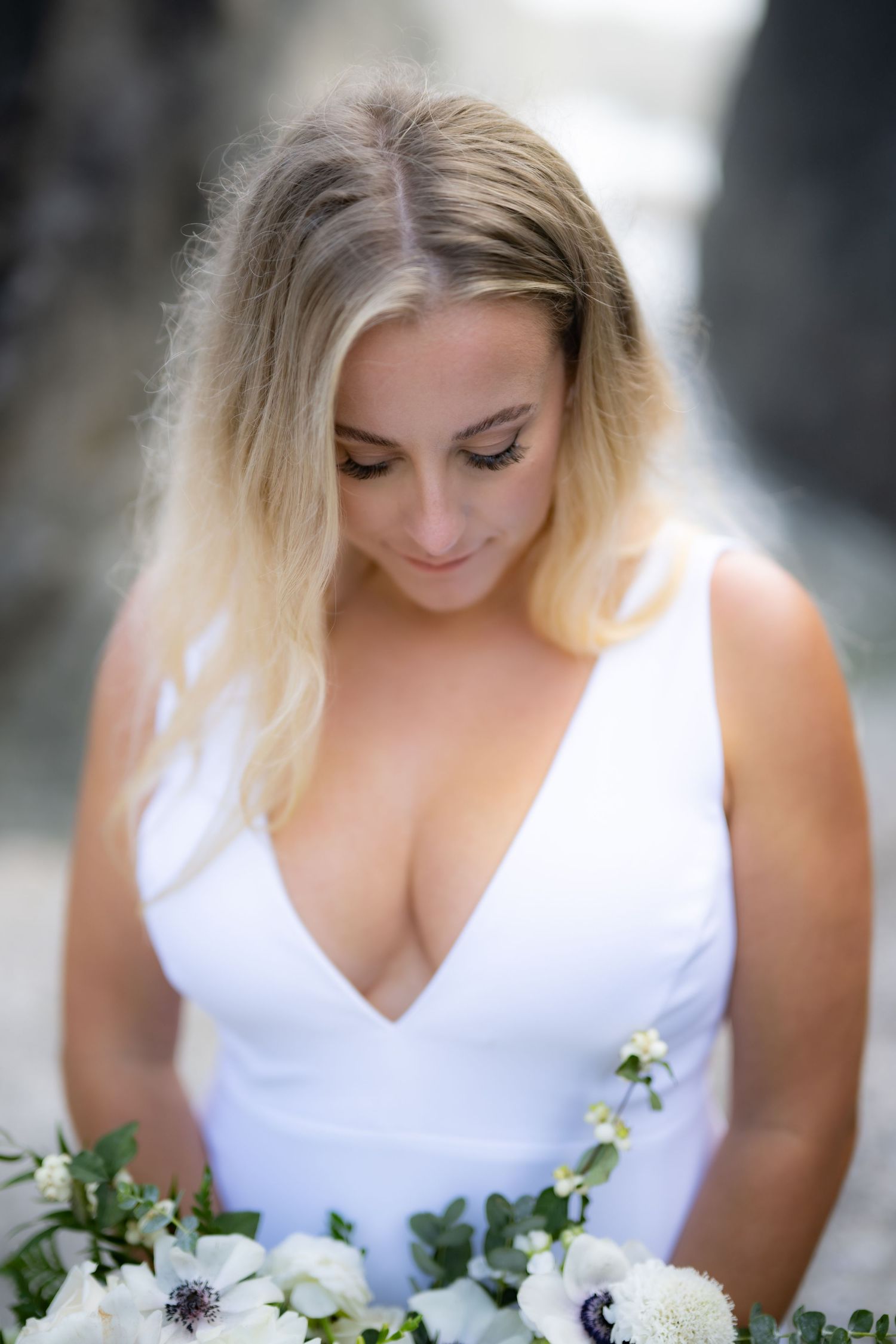 Bride in white dress holds elegant bouquet of white flowers against blurred background.