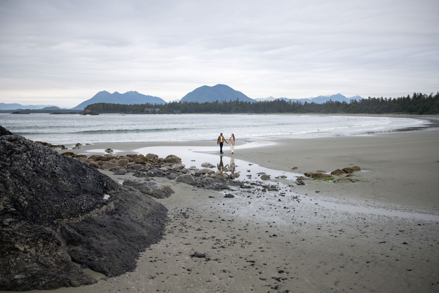 Panoramic view of a secluded beach with mountains and dramatic cloudy sky.