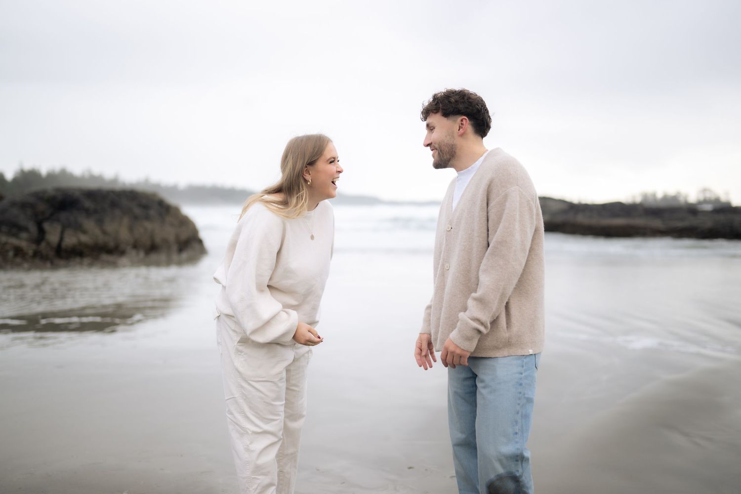 Couple in neutral sweaters sharing an intimate moment on a cloudy beach.