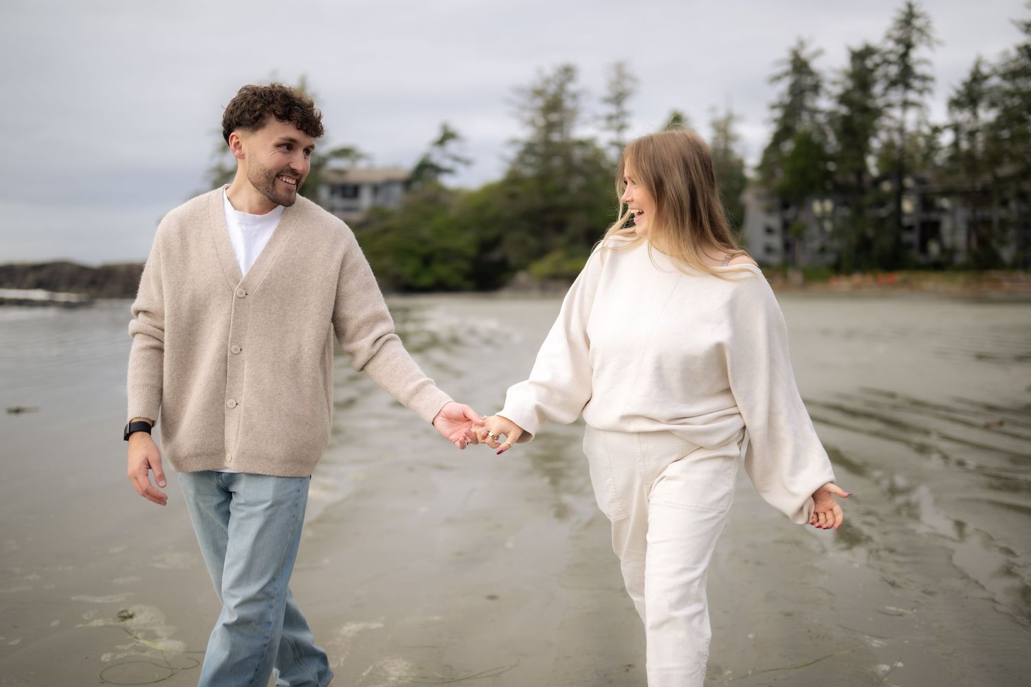 Couple walking hand in hand along a misty Pacific Northwest beach.