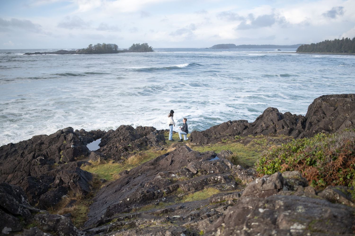 A lone figure stands on rocky coastal cliffs overlooking the Pacific Ocean waves.