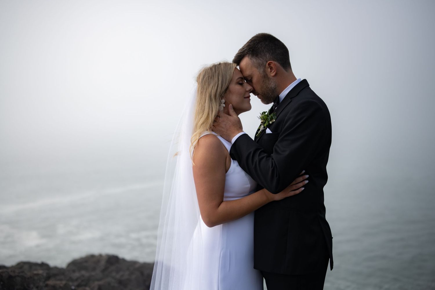 A tender moment between a couple against a misty coastal backdrop.