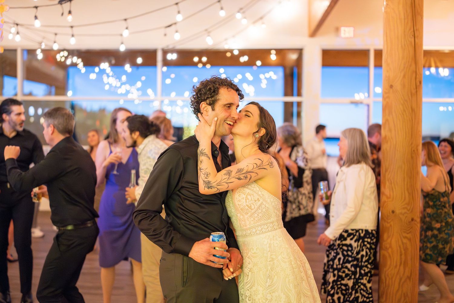 Couple shares a romantic dance moment under string lights at an indoor wedding reception.