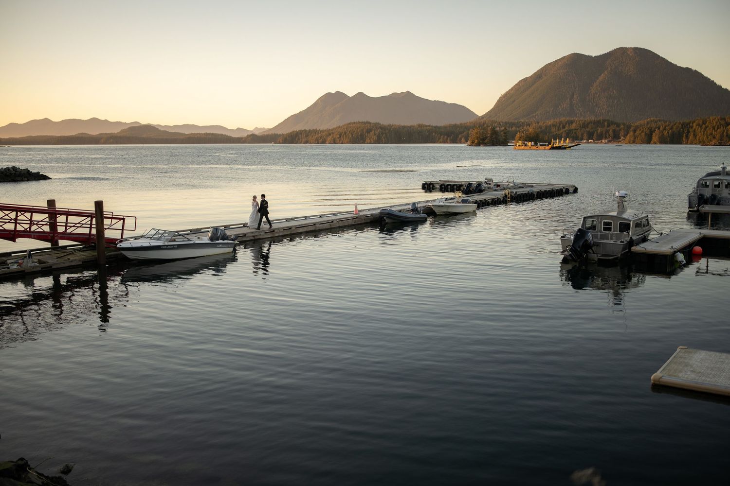 Scenic marina at sunset with boats docked along wooden piers against mountain backdrop.