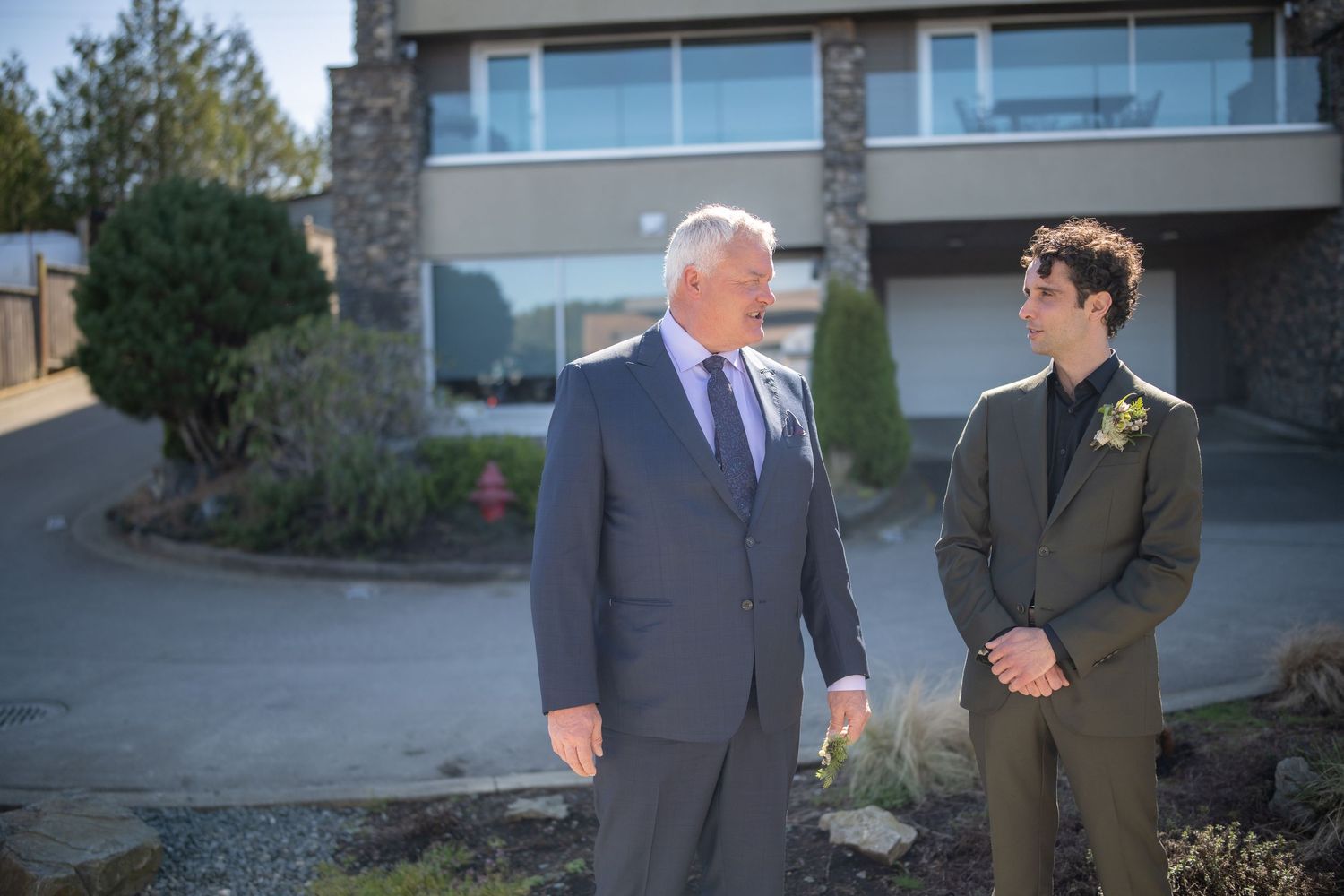 Formal event attendees in suits standing outside modern building.