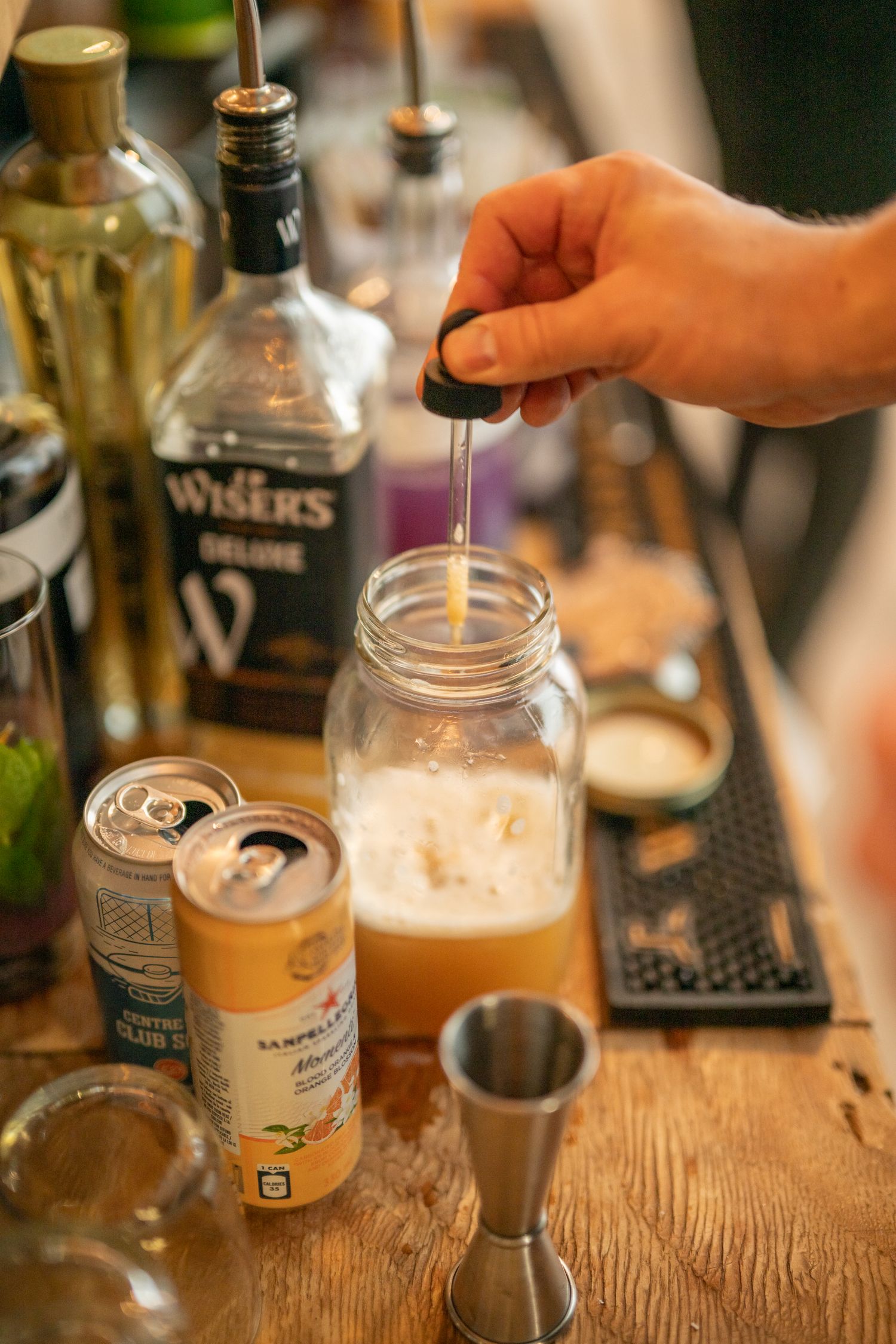 Bartender pouring craft cocktails at a rustic wooden bar setup.