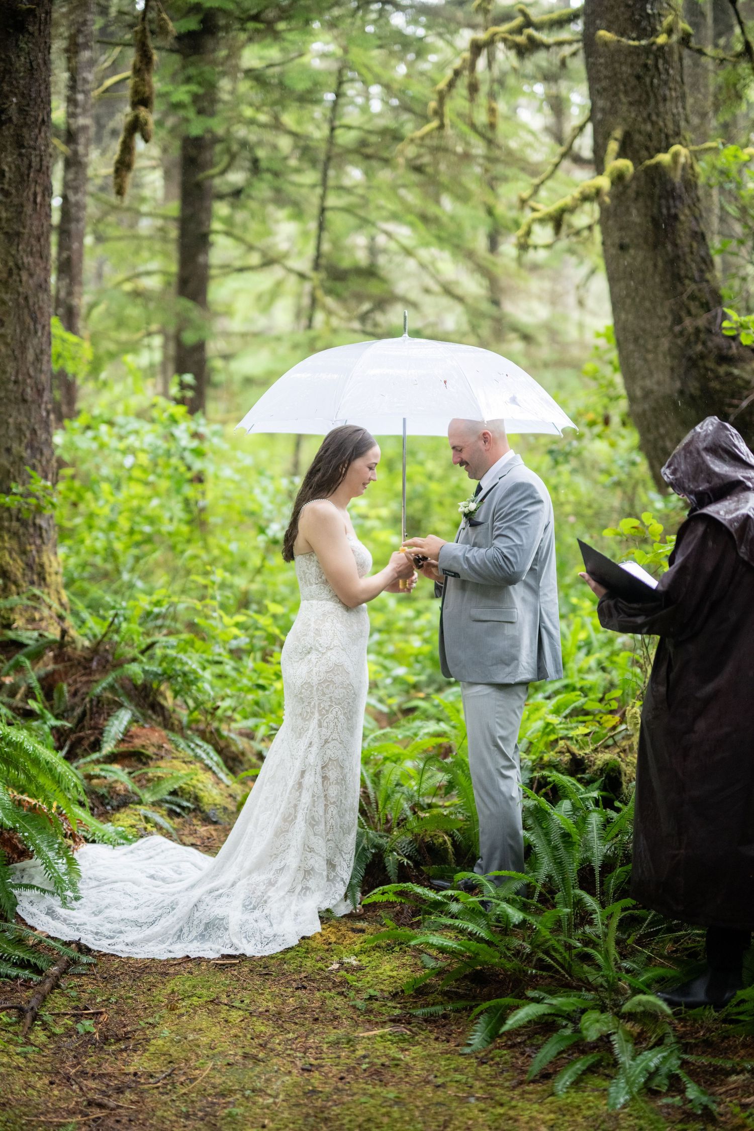 An intimate forest wedding ceremony with attendees holding white umbrellas among tall trees.