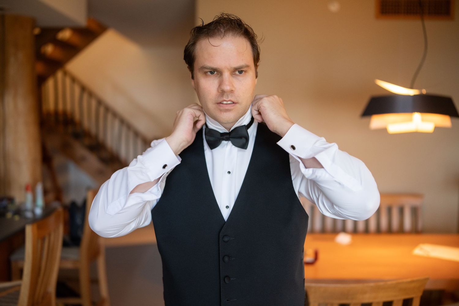 Person in formal wear adjusting bowtie and cuffs before event.