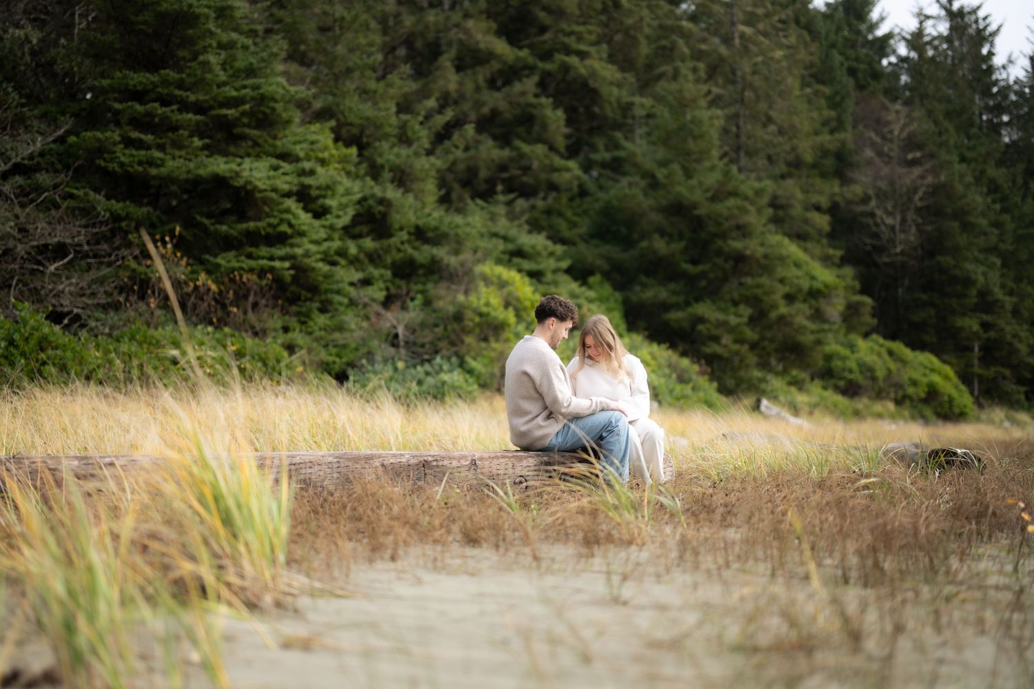 A couple walks together through a scenic forest path surrounded by tall evergreen trees.