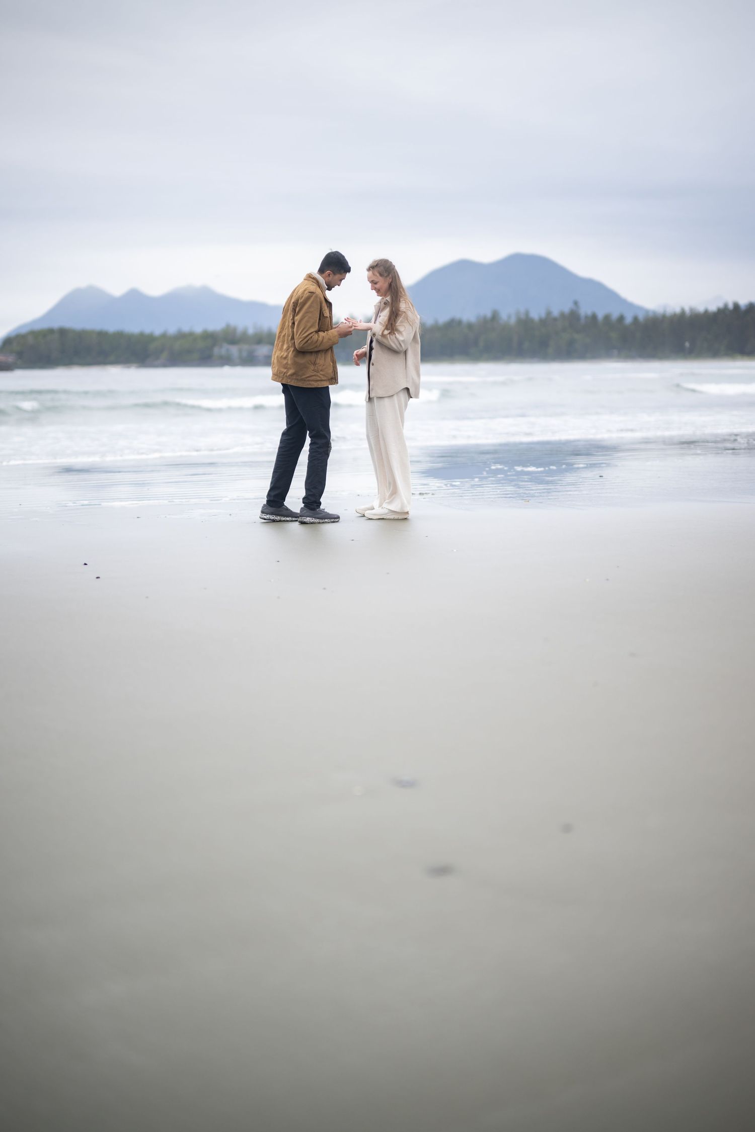 Intimate moment shared on a secluded Pacific Northwest beach with mountain views.
