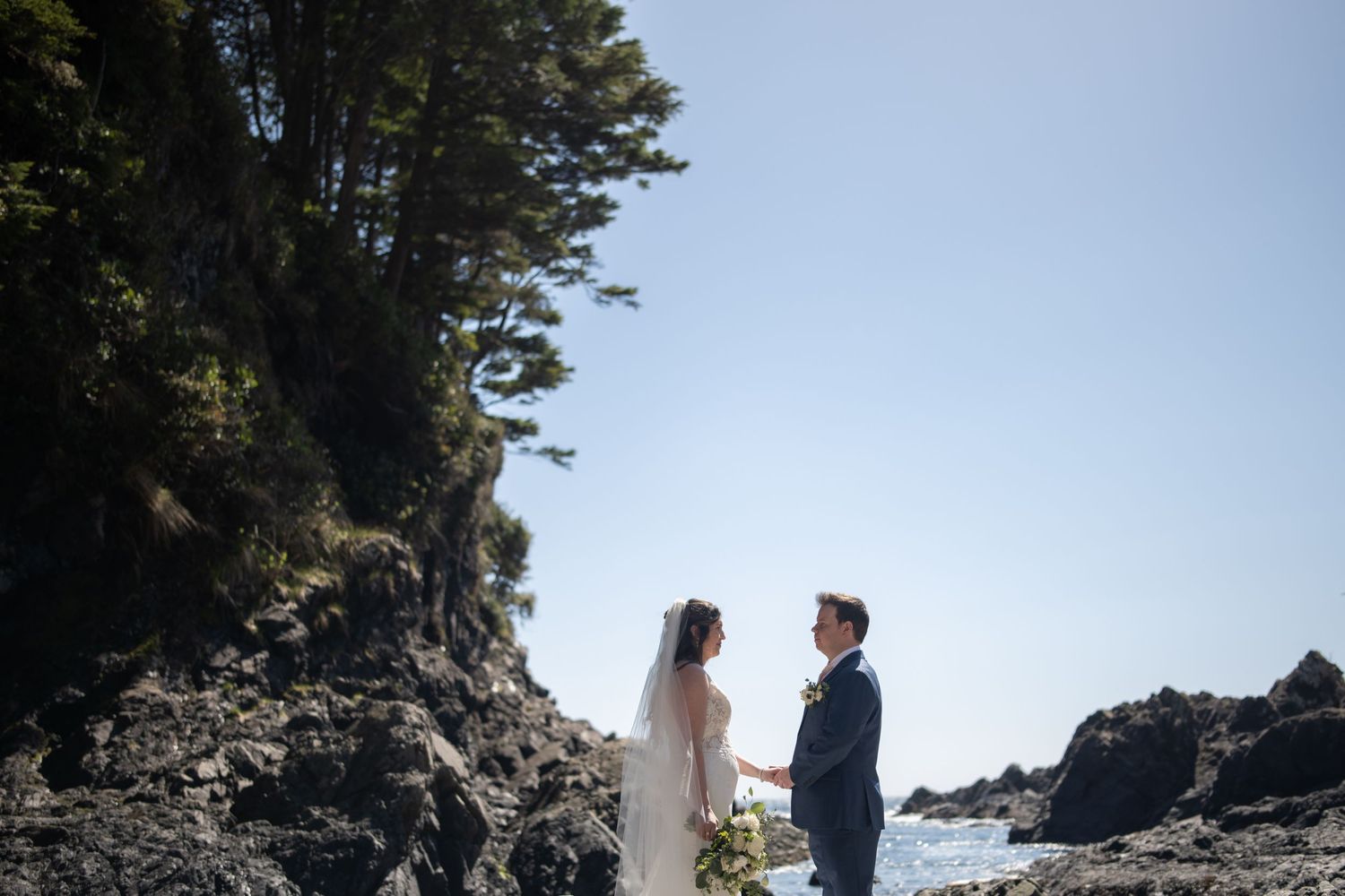 Coastal wedding ceremony with distant figures against dramatic rocky cliffs and ocean.